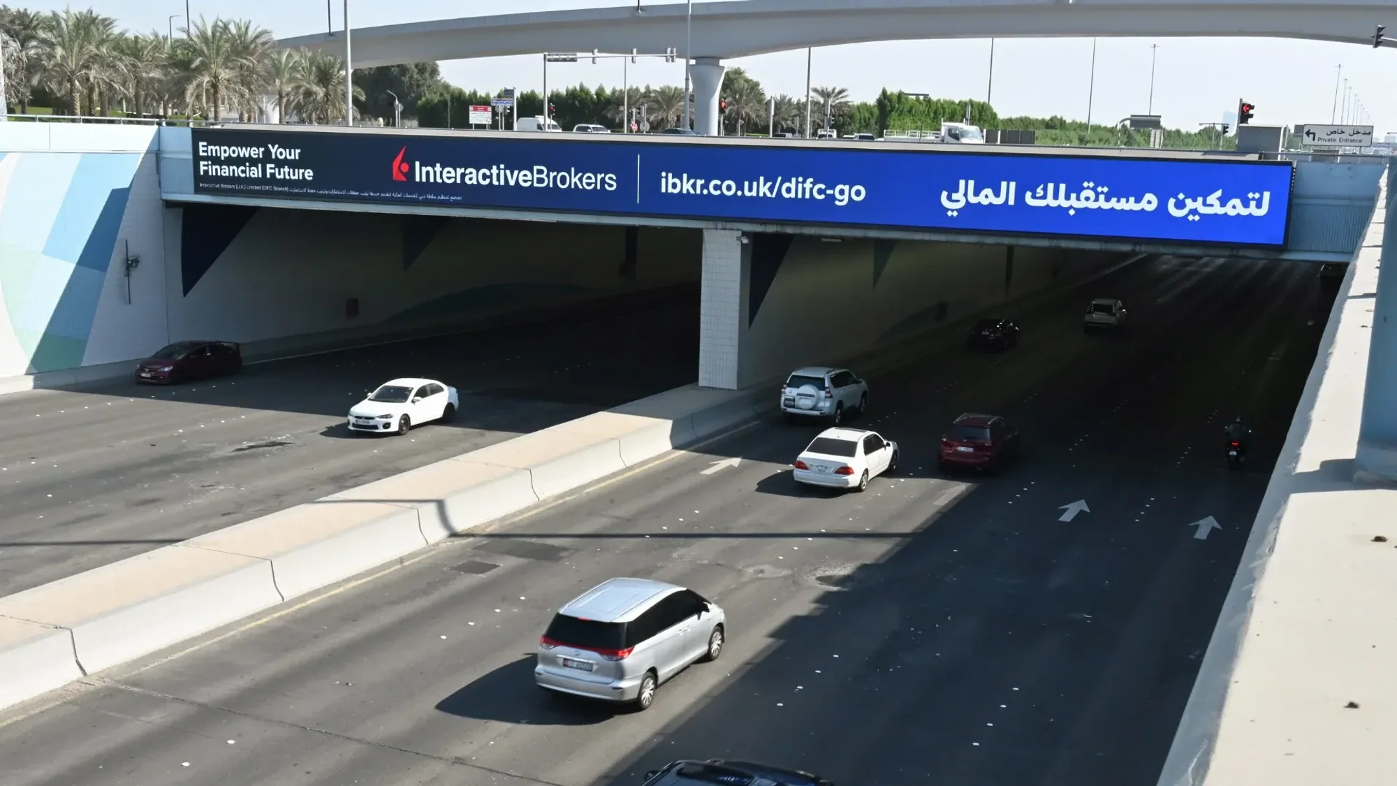 Bridge banner advertising: an Interactive Brokers banner spans a highway underpass above moving traffic.