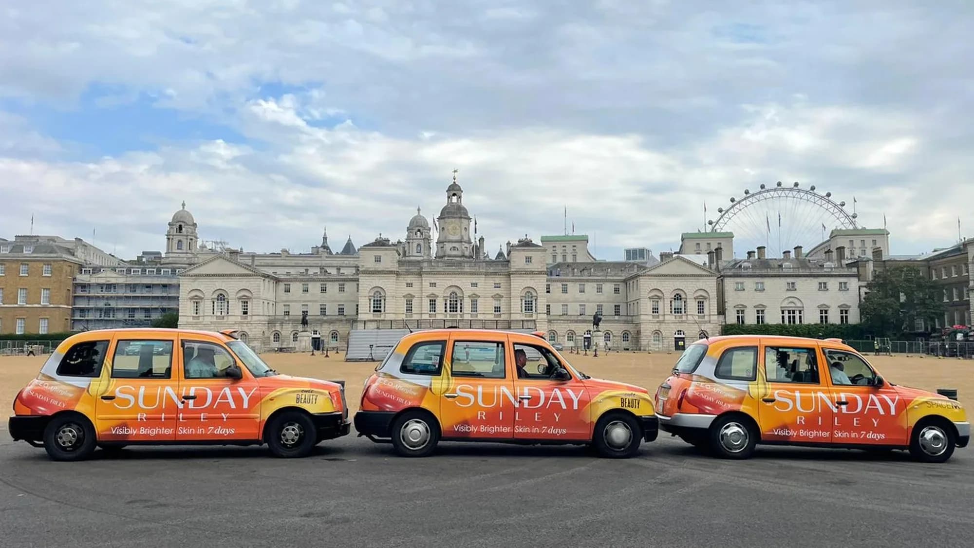 Taxi advertising in London, in the United Kingdom: three Sunday Riley taxis stand before a white building and the London Eye.