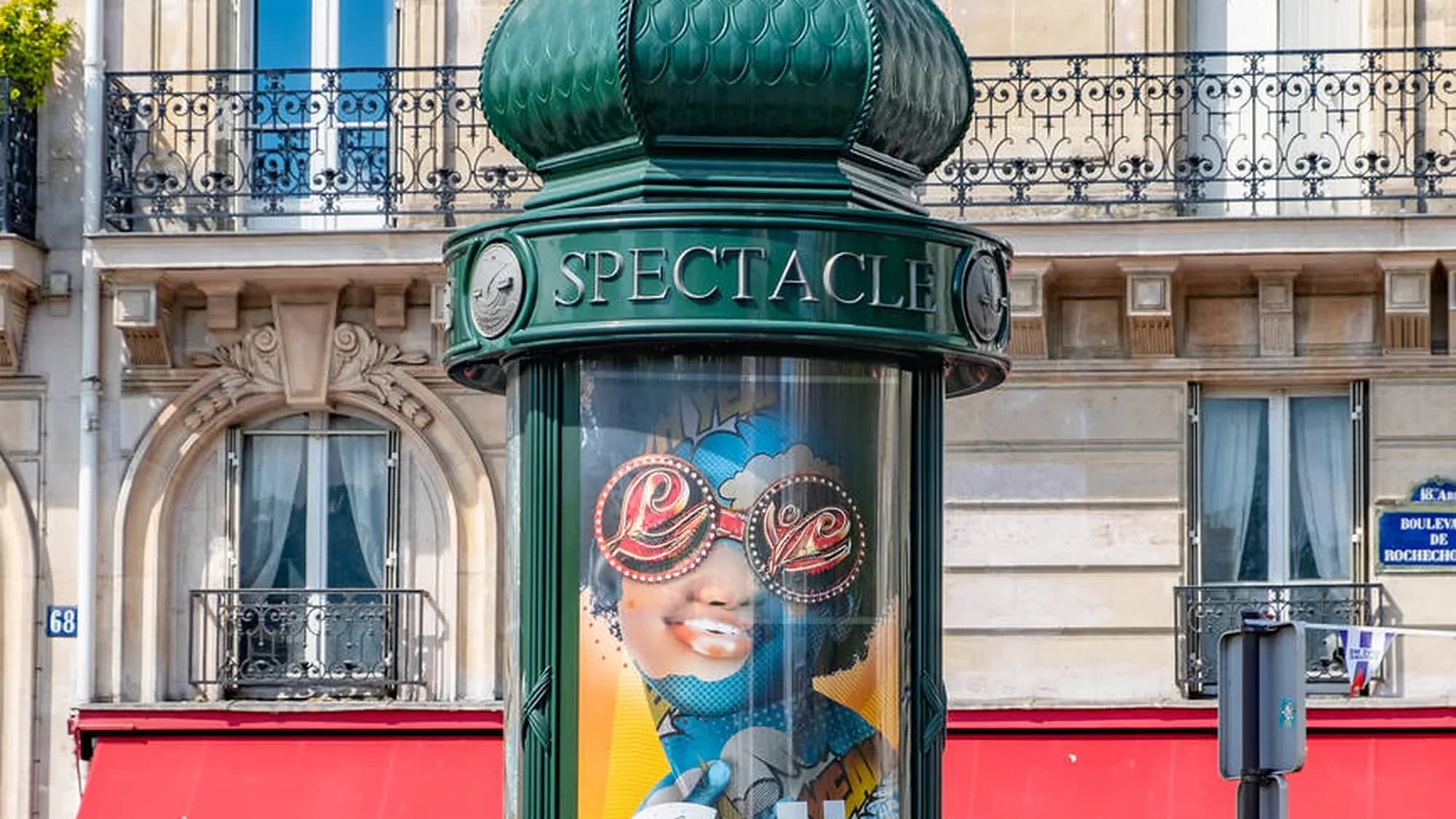 Street furniture advertising in Paris, France: a green spectacle column on Boulevard de Rochechouart displays a poster of a woman wearing Love sunglasses.