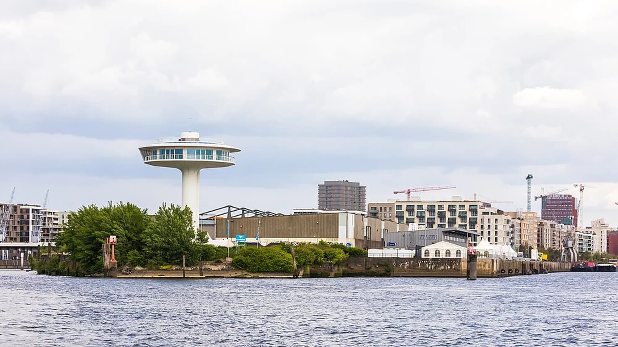 The Lighthouse Zero tower in Hamburg, Germany: a white disc-topped tower stands on a harbour peninsula, with cranes and new apartment blocks behind it.