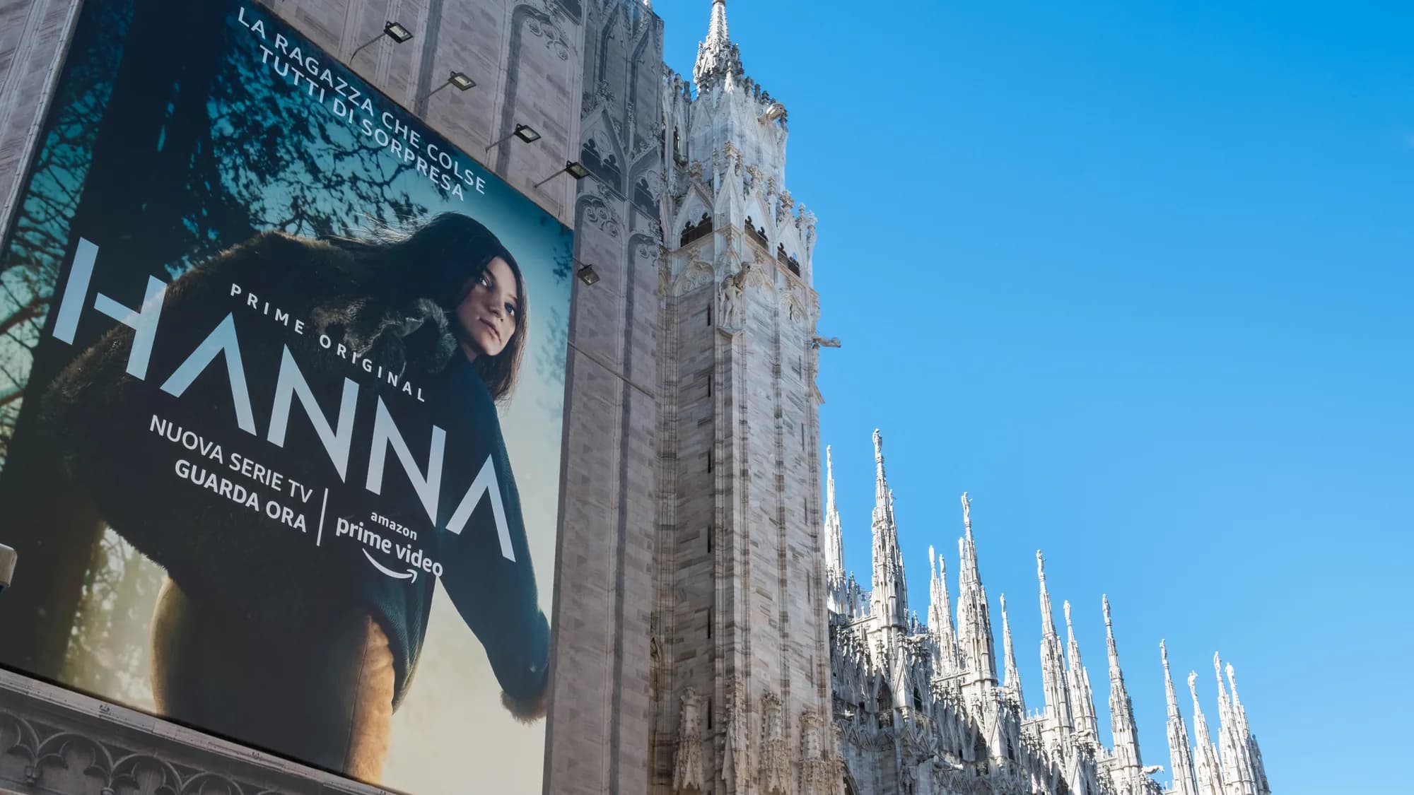 The Duomo in Milan, Italy: statues along the roof frame a view down a pedestrian street, with a small screen far ahead.