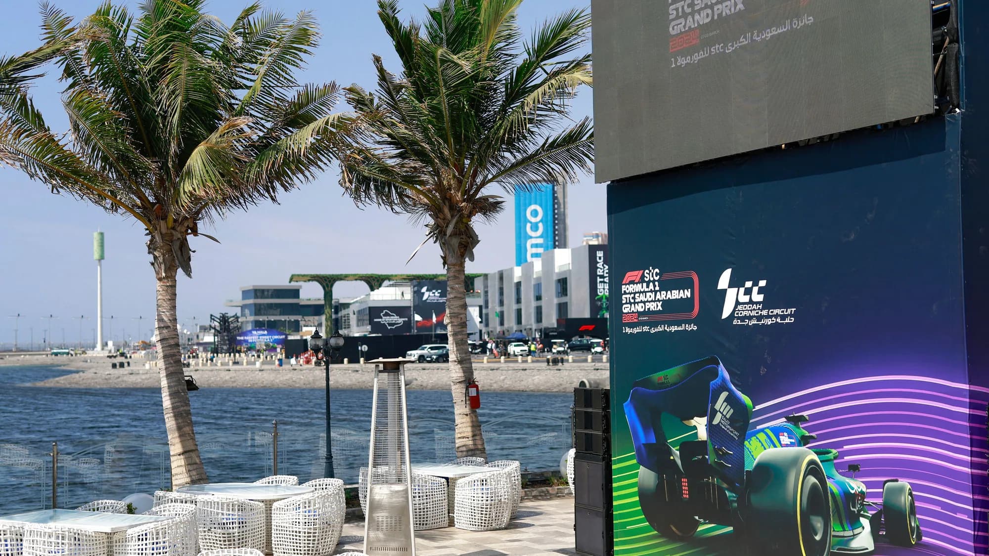 Outdoor advertising on the Jeddah Corniche in Saudi Arabia: an STC Formula 1 Saudi Arabian Grand Prix board stands among palms and waterfront tables.