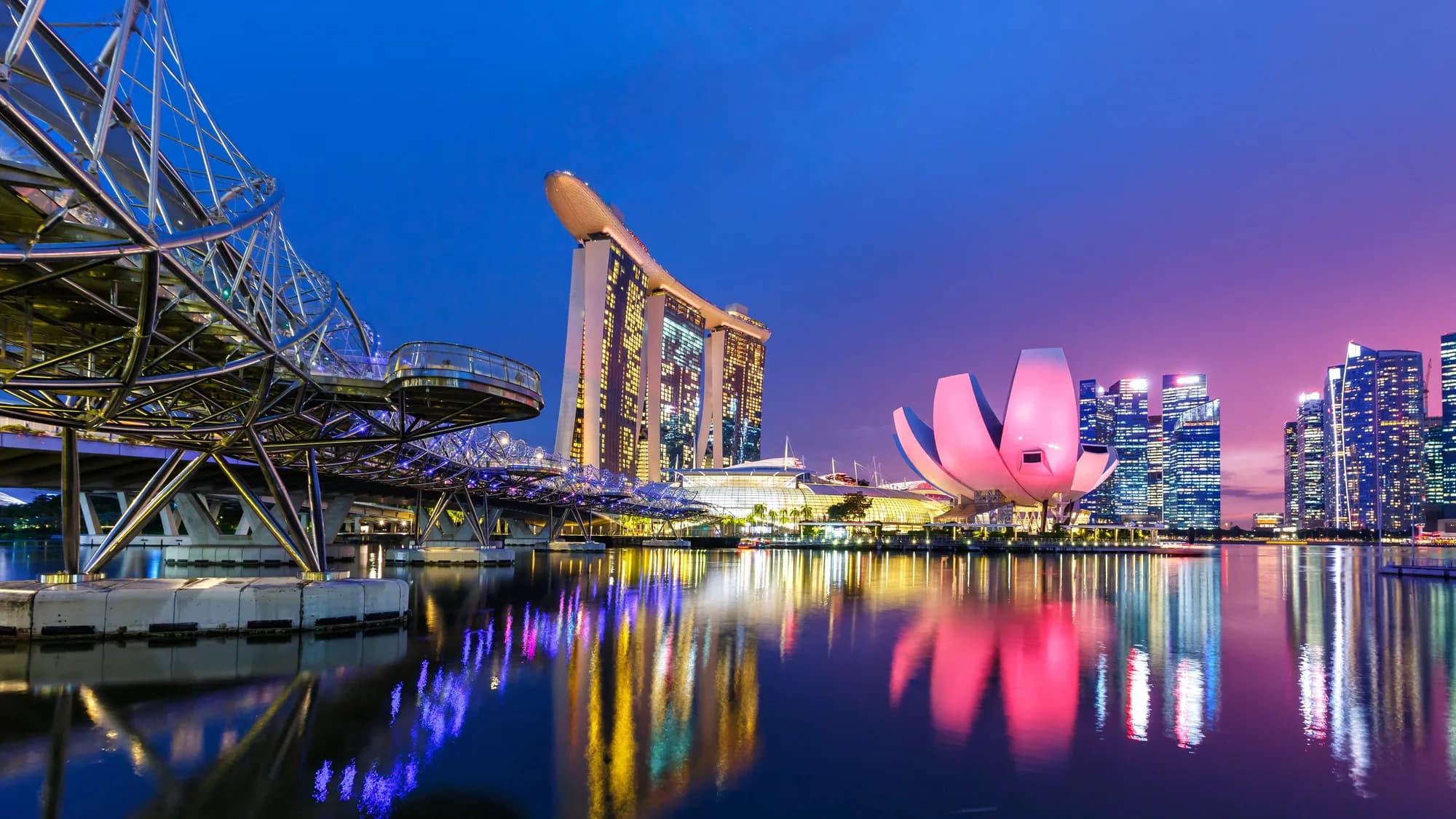 Outdoor advertising at Marina Bay in Singapore: people walk the promenade past 7-Eleven banners, with the financial district towers across the water.