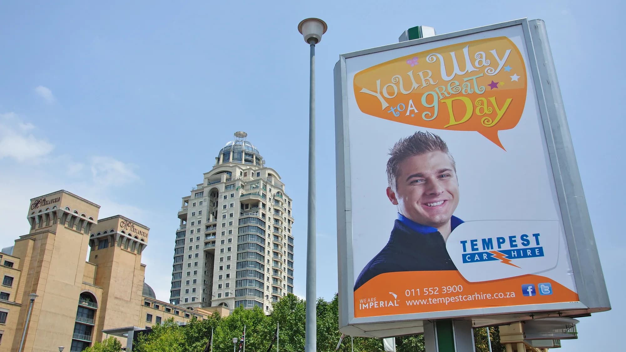 Outdoor advertising in Sandton, Johannesburg: a Tempest Car Hire poster reading your way to a great day stands in front of a domed tower.