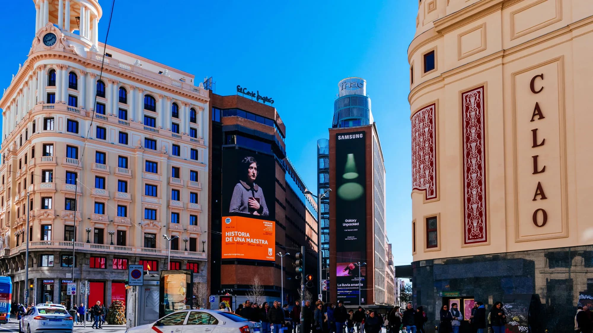 Digital billboard advertising at Plaza del Callao in Madrid, Spain: the Callao facade faces Samsung and El Corte Inglés screens, one titled Historia de una maestra.