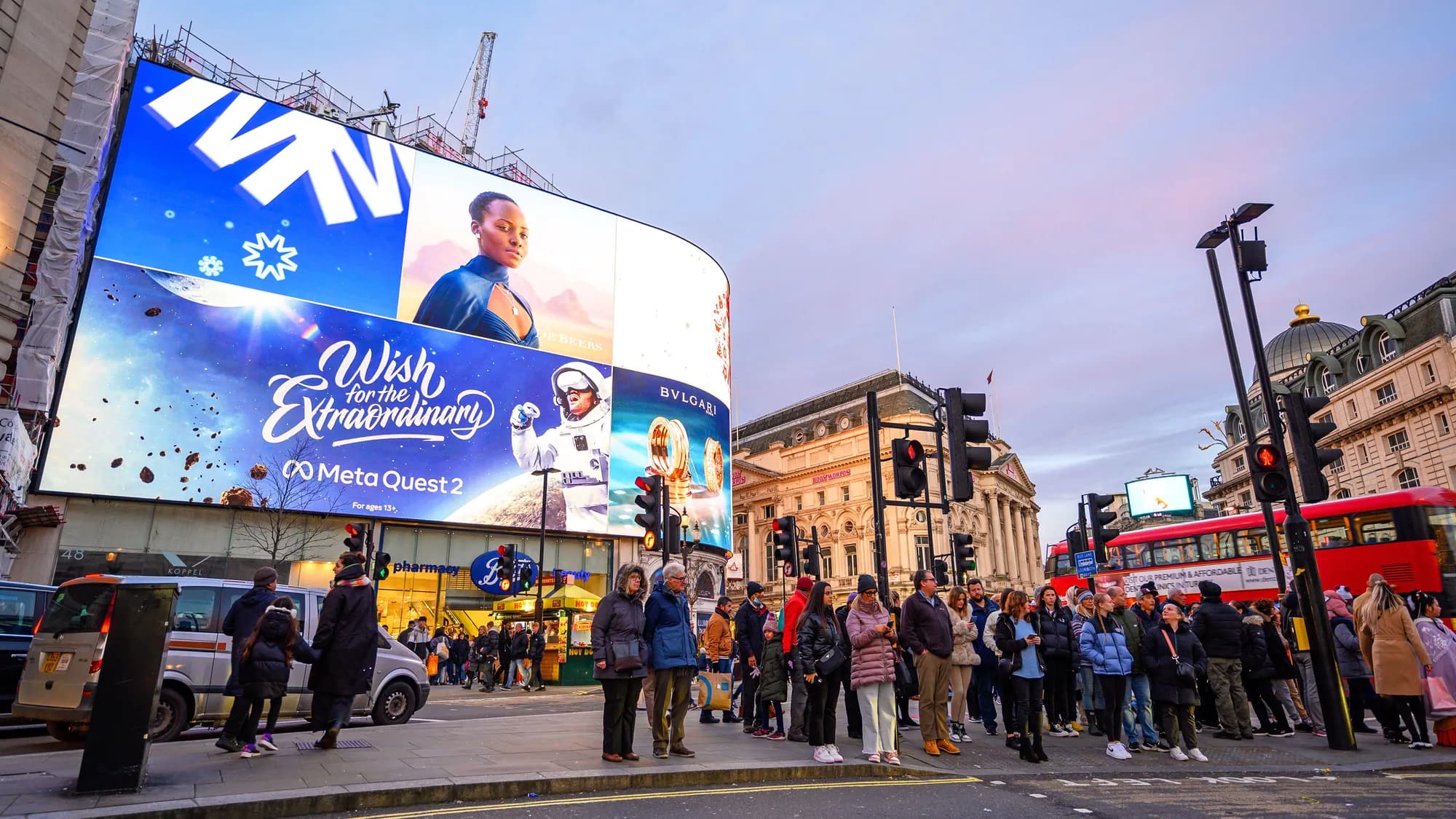 Digital billboard advertising at Piccadilly Circus in London, in the United Kingdom: curved screens show a Meta Quest 2 advert, Coca-Cola and Bvlgari above a Boots store, with a crowd and a red bus in front.