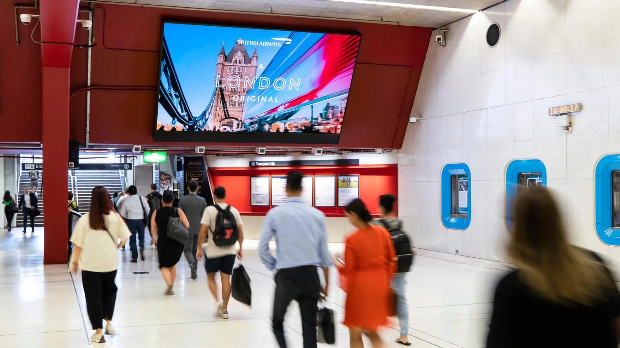 Digital out-of-home advertising in an Australian station: commuters pass a digital screen showing British Airways' A London Original, over Tower Bridge.