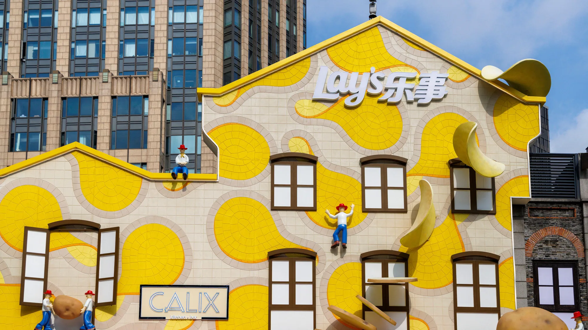 A brand activation in China: a building facade is wrapped for Lay's, with giant crisps, potatoes and small climbing figures.