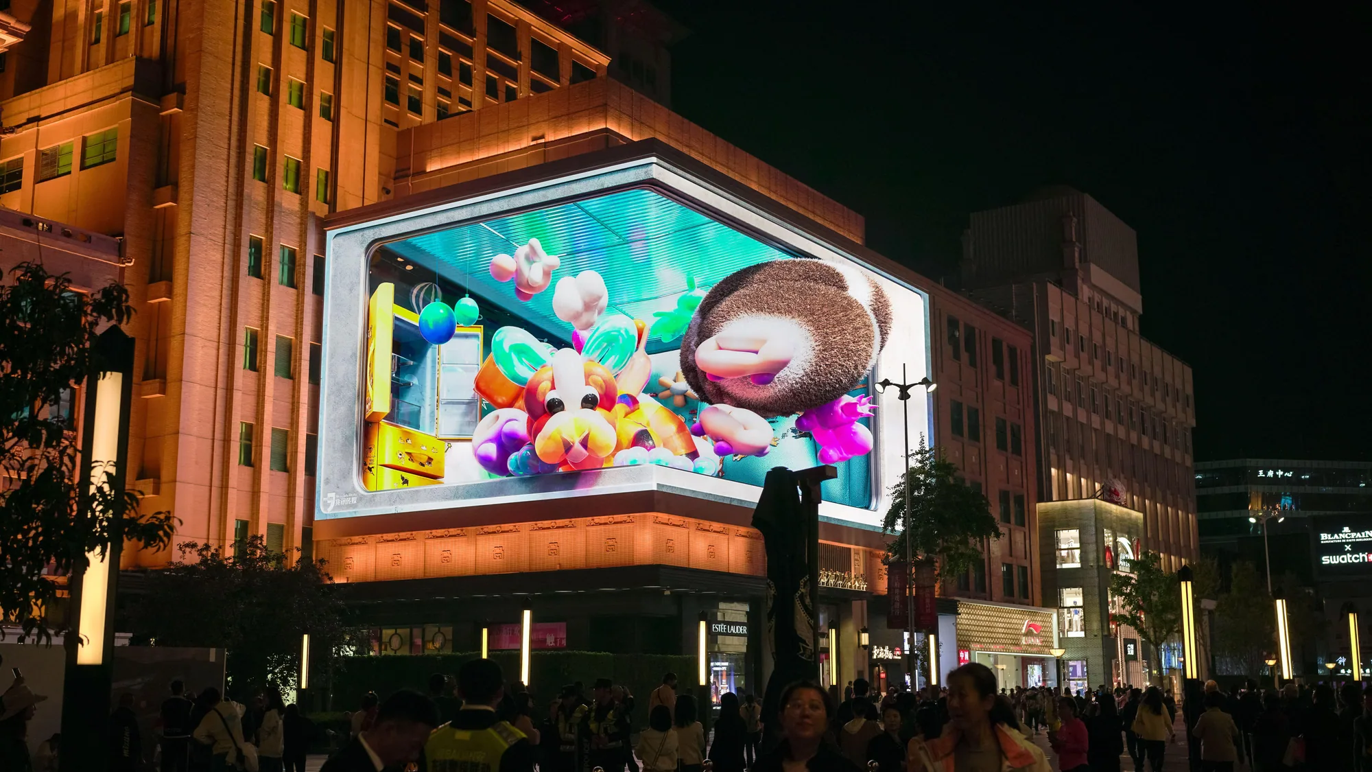 Digital out-of-home advertising in China: a corner screen at night shows a cartoon dog and a chocolate roll above a crowded shopping street.