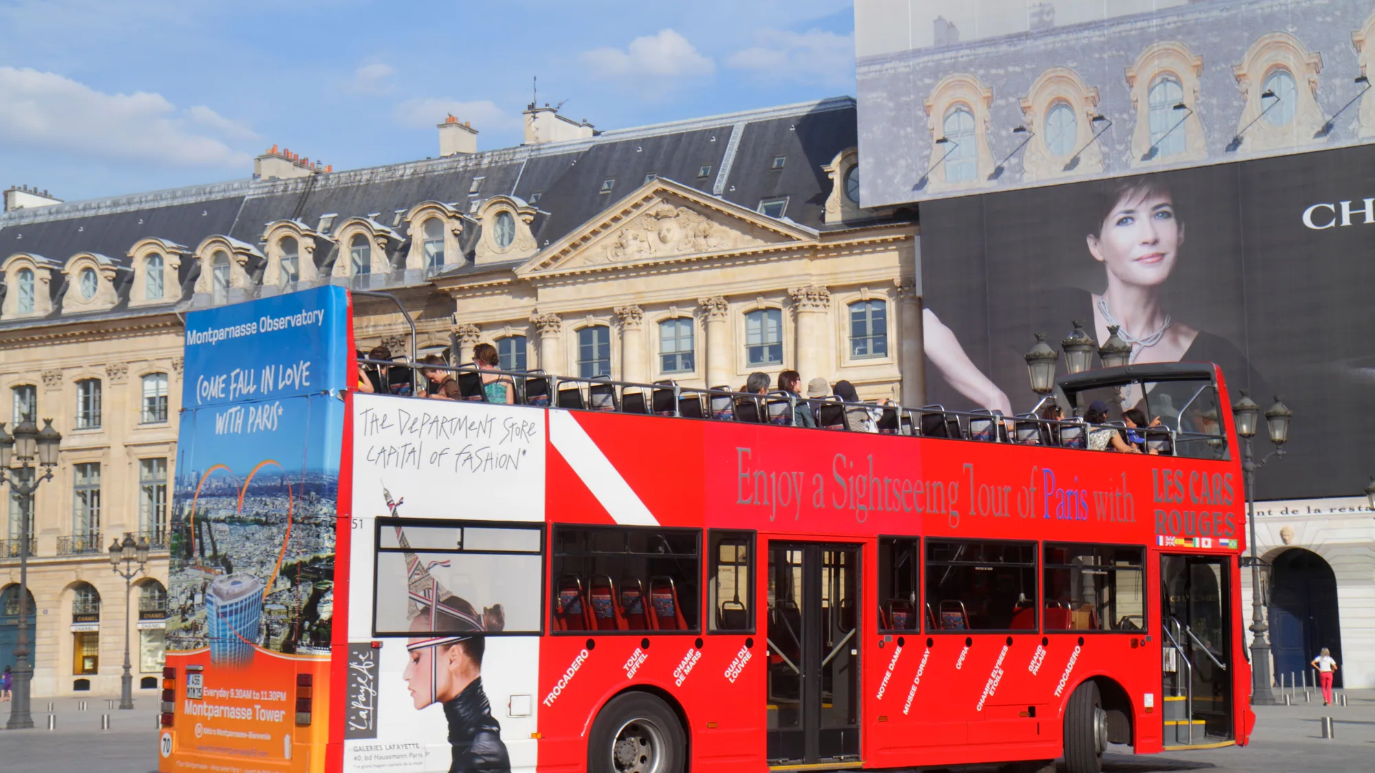 Bus advertising in Paris, in France: a red Les Cars Rouges open-top bus advertises a sightseeing tour, in front of a Chanel building poster.