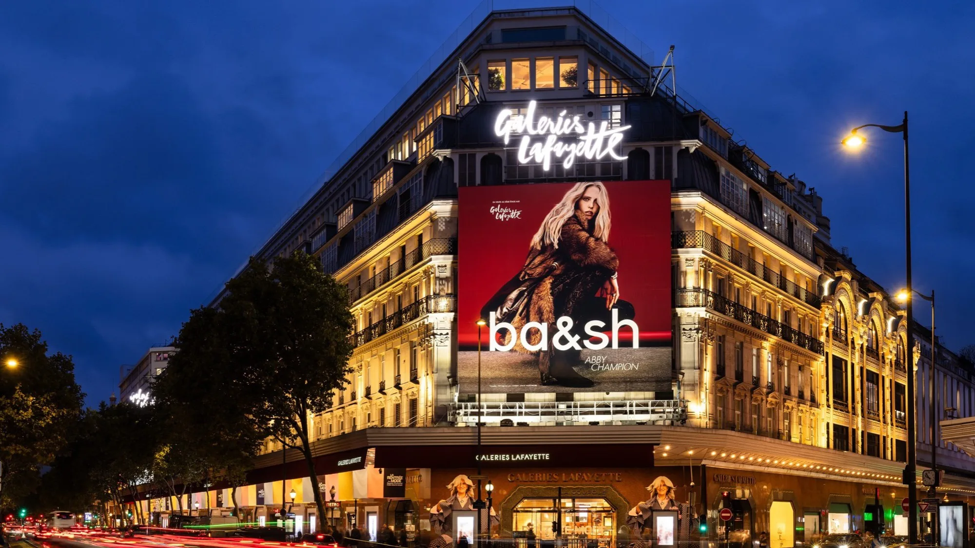 Digital out-of-home advertising in Paris, in France: a ba&sh screen with Abby Champion covers the Galeries Lafayette facade at night.