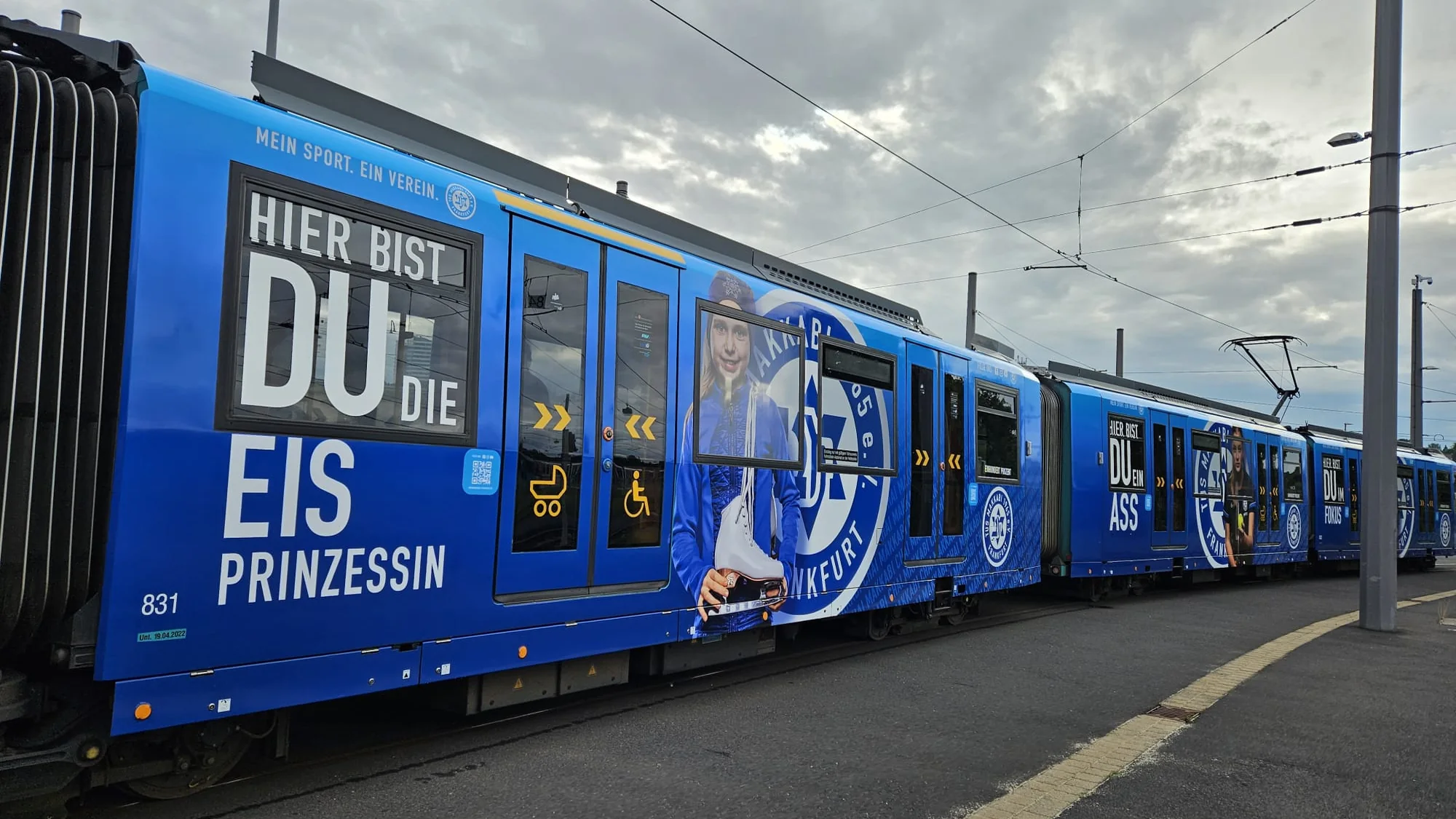 Tram advertising in Frankfurt, Germany: a blue train at an outdoor platform reads Hier bist du die Eisprinzessin, with a skater on the side.