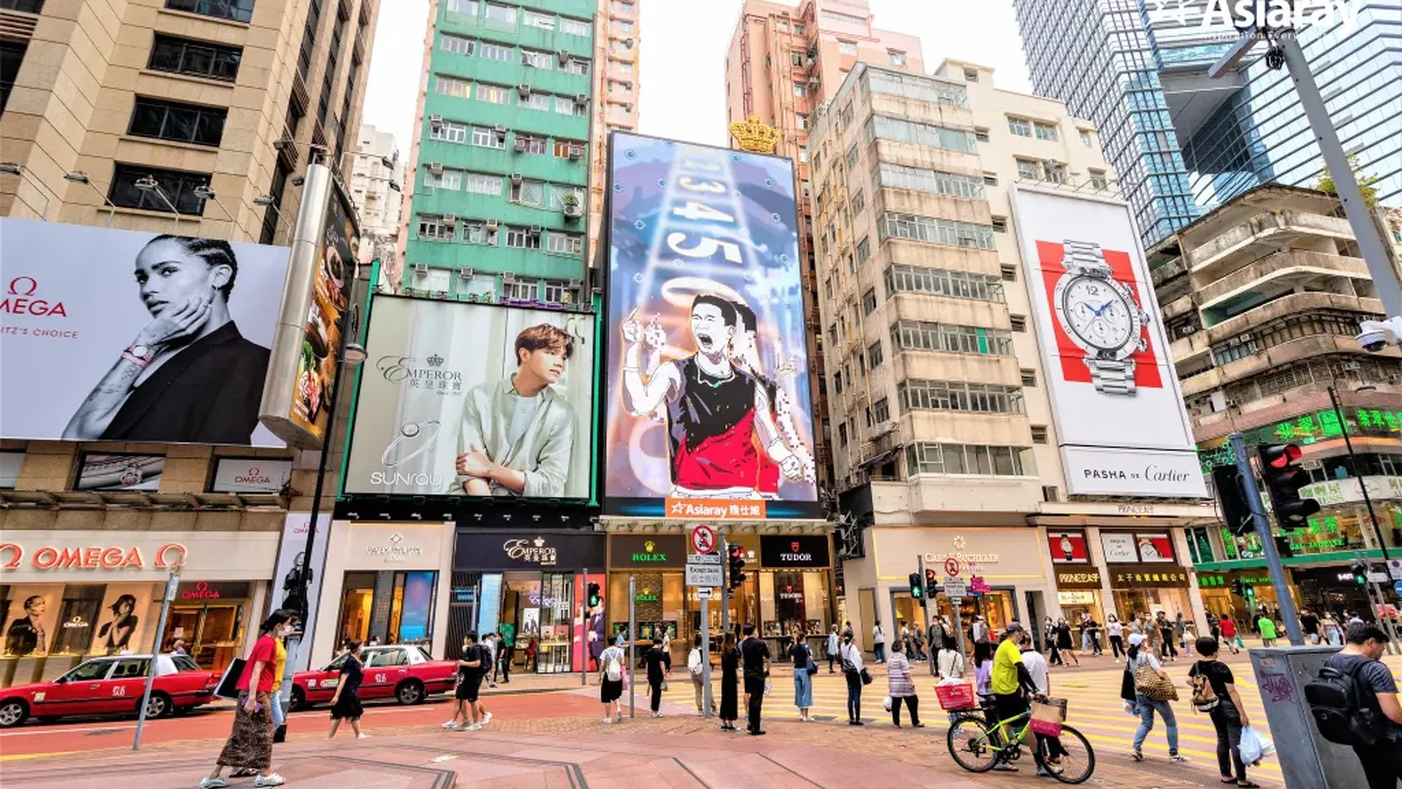 Large format billboard advertising in Hong Kong: giant watch boards, including Omega, Emperor and Cartier, rise over a crowded crossing with red taxis.