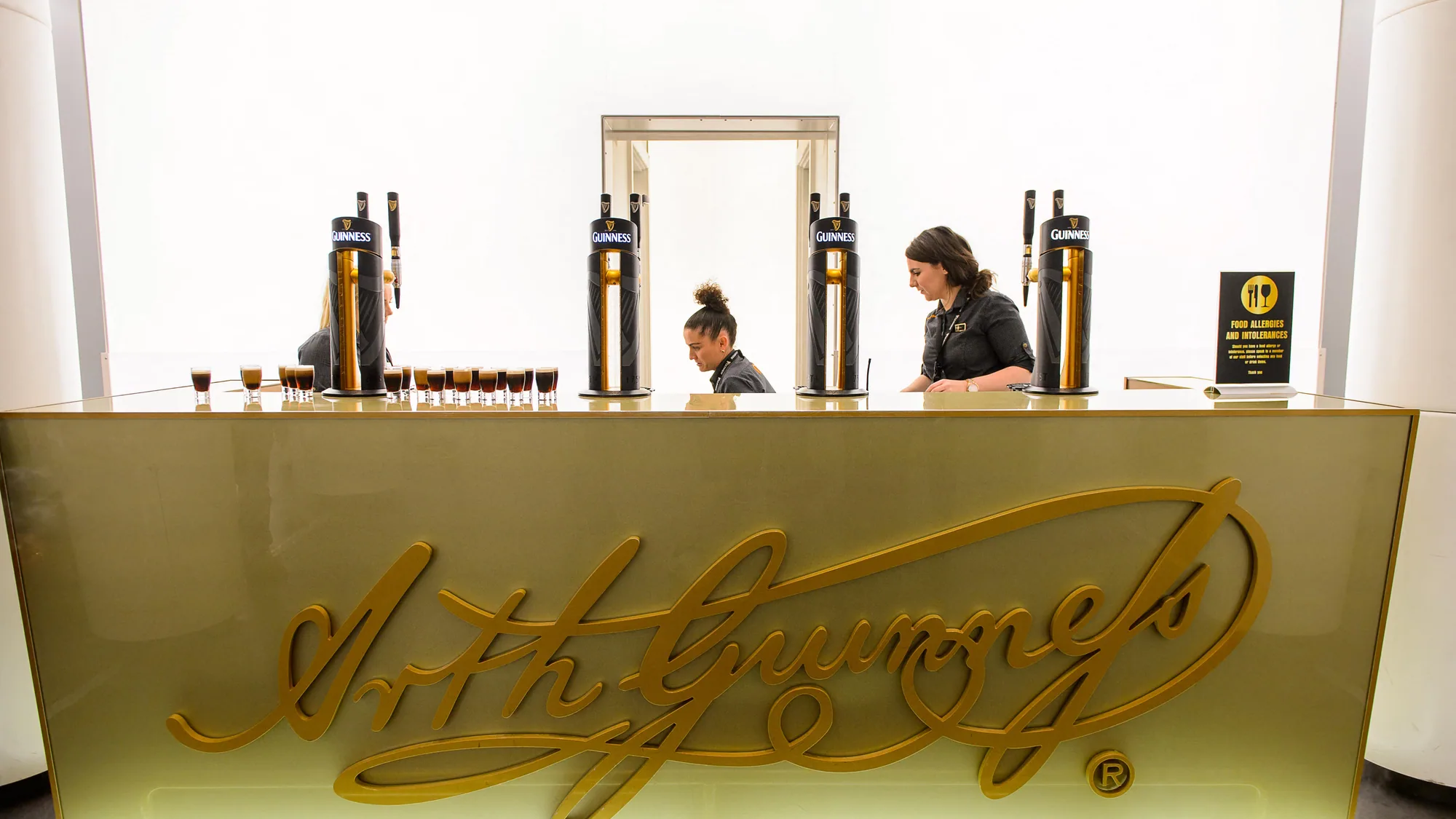 A Guinness brand activation in Ireland: a tasting bar carries a gold Arthur Guinness signature across the counter, with harp taps lined up behind it.