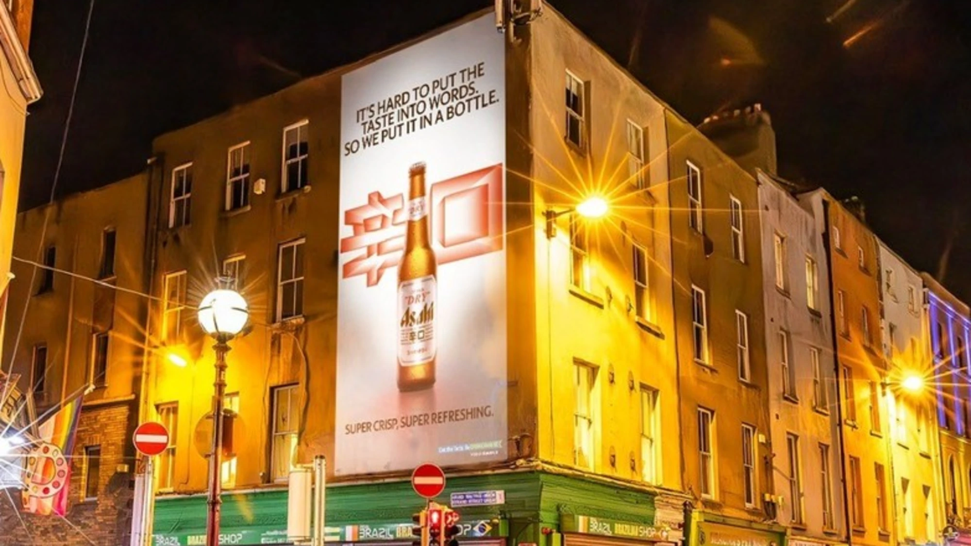 Building banner advertising in Ireland: an Asahi Super Dry banner at night reads, It's hard to put the taste into words, so we put it in a bottle.