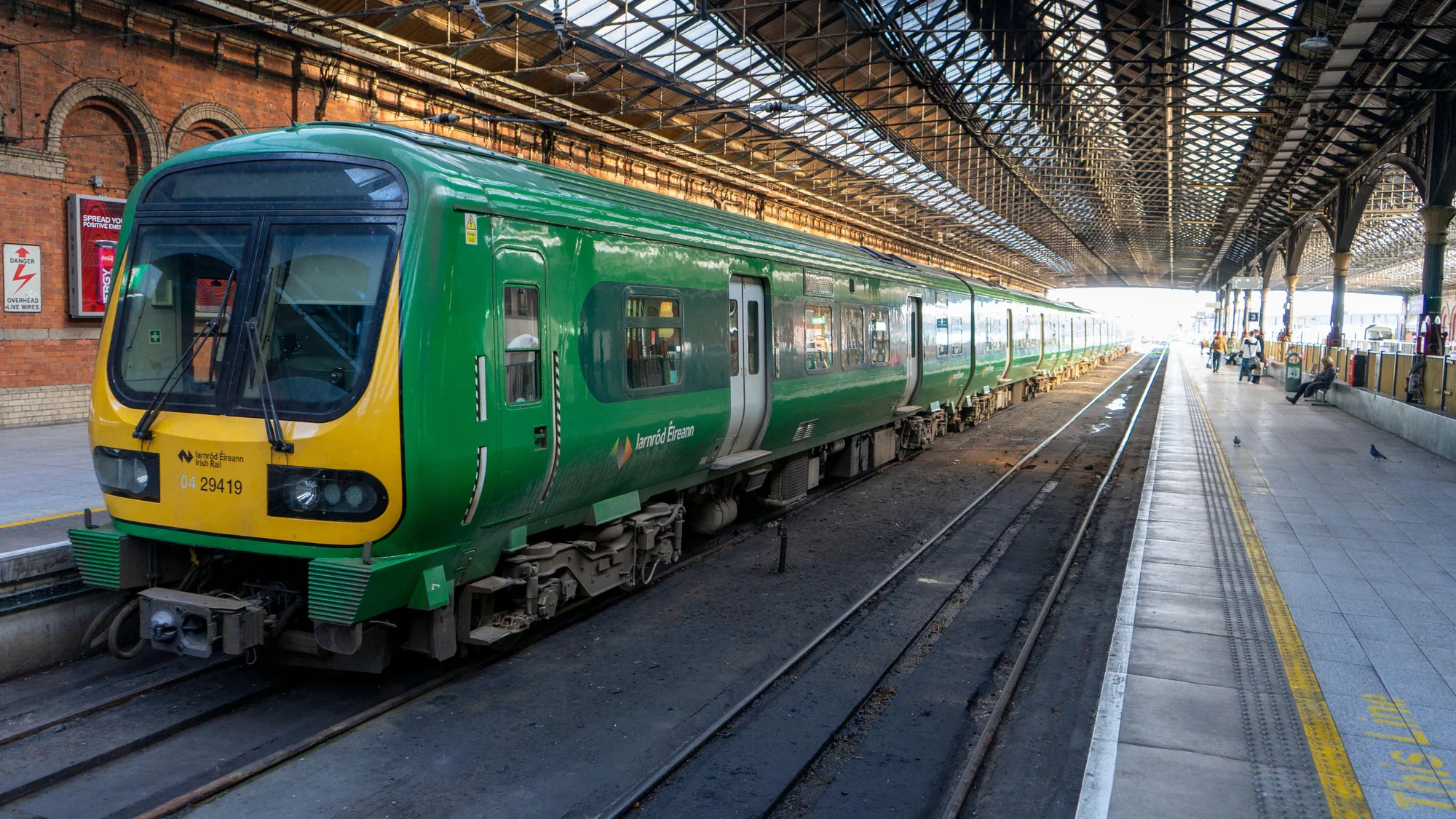 An Iarnród Éireann train in Ireland: a green and yellow carriage stands at a covered station platform.