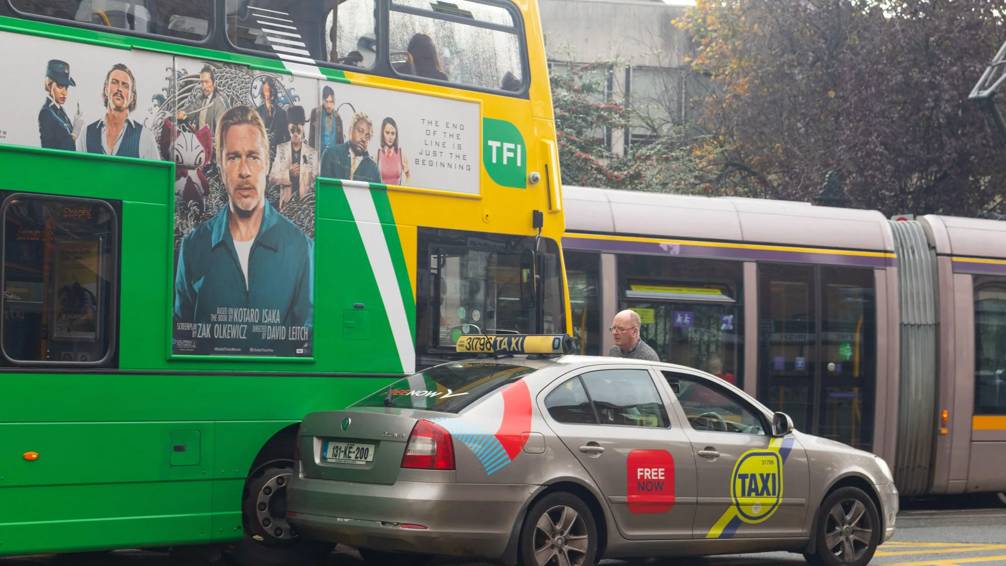 Taxi advertising in Ireland: a Free Now taxi sits beside a TFI double-decker bus poster reading The end of the line is just the beginning, with a tram behind.