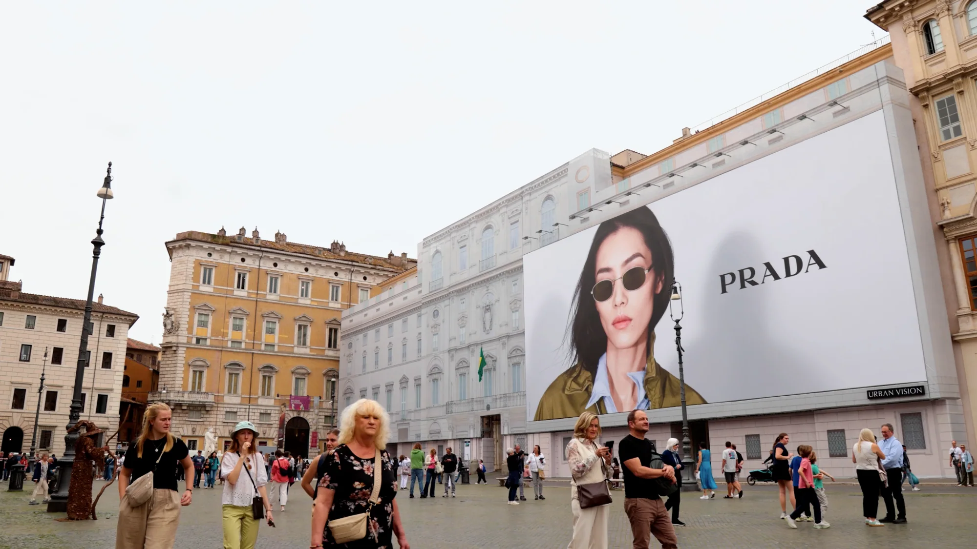 Billboard advertising in Italy: a large Prada board of a woman in sunglasses faces a crowded square.