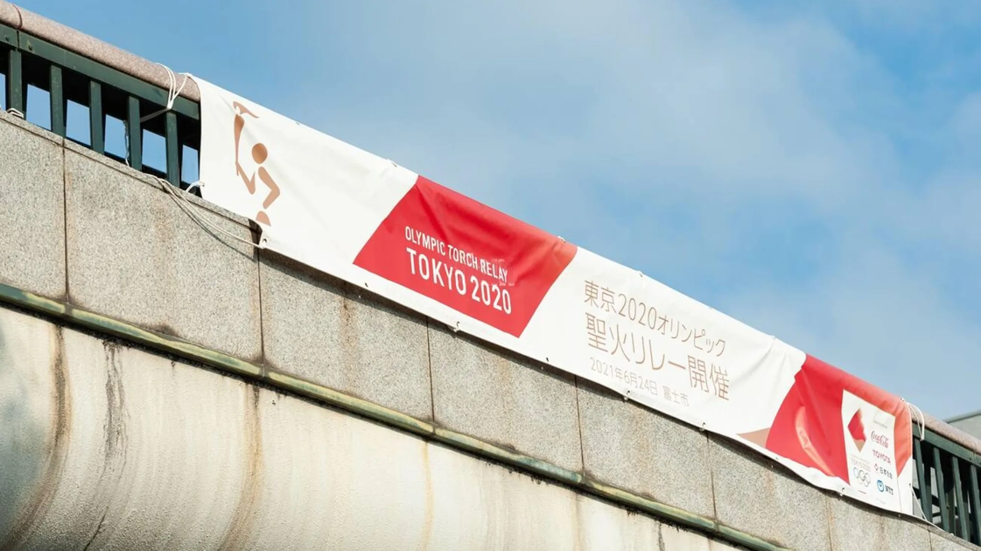 Bridge banner advertising in Tokyo, Japan: a red and white banner on a concrete overpass reads Olympic Torch Relay Tokyo 2020.