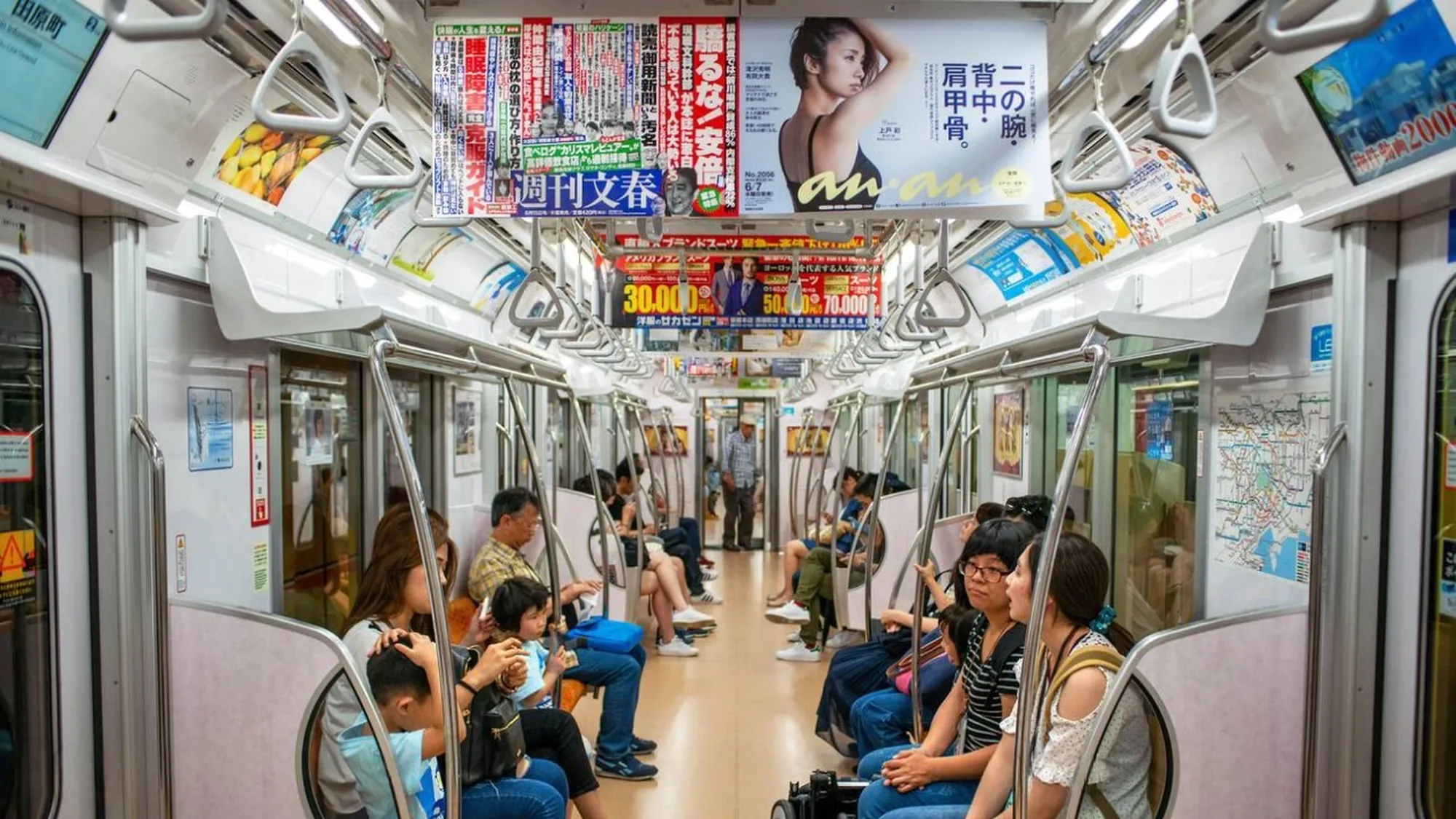 Metro advertising in Japan: hanging cards inside a crowded carriage include an anan poster and a 週刊文春 panel above the seats.
