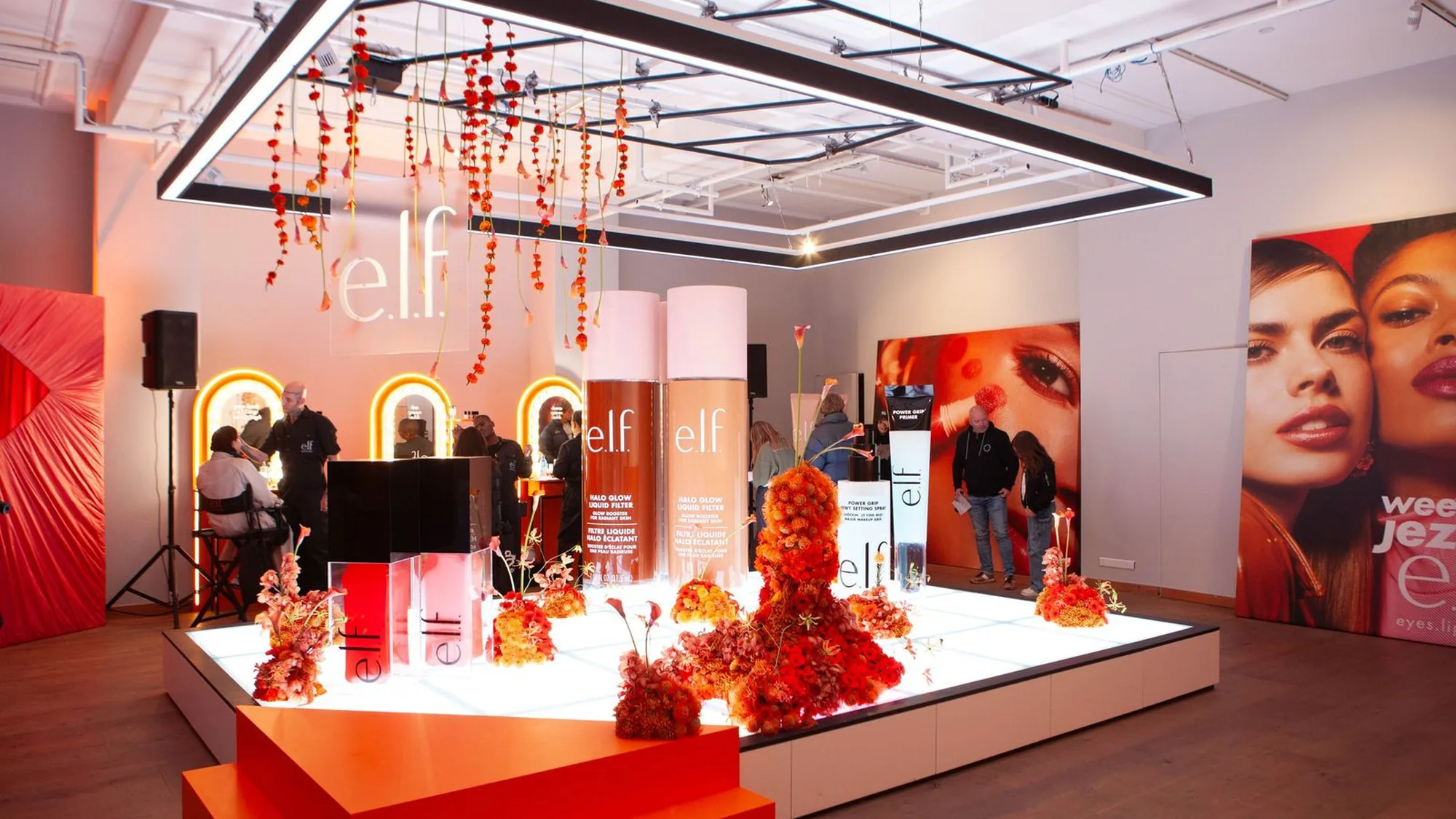 A brand activation in the Netherlands: an e.l.f. stand with oversized foundation bottles and orange flowers sits under a hanging light, beside a wall portrait.