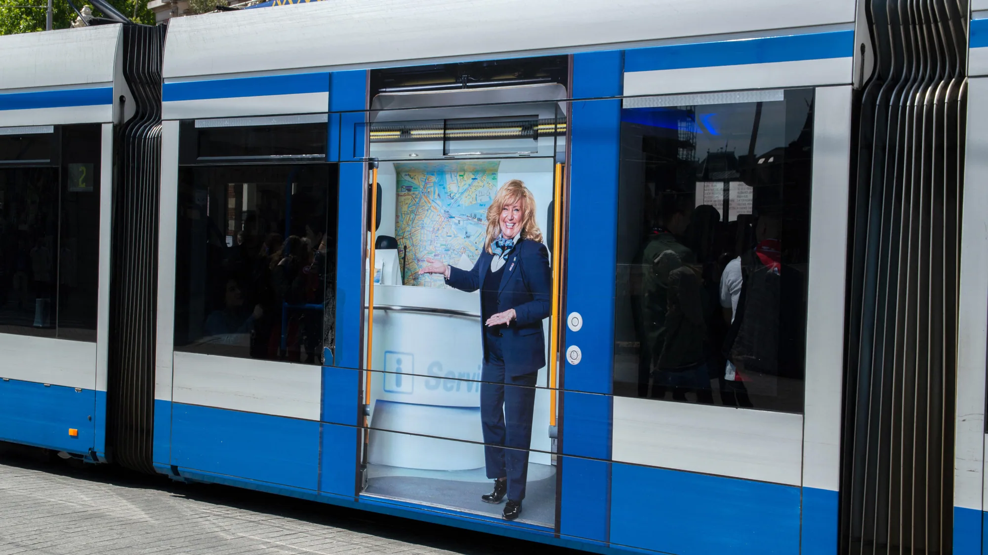 Tram advertising in Amsterdam, the Netherlands: a blue and white tram carries a full-height side advert of a woman at an information counter.