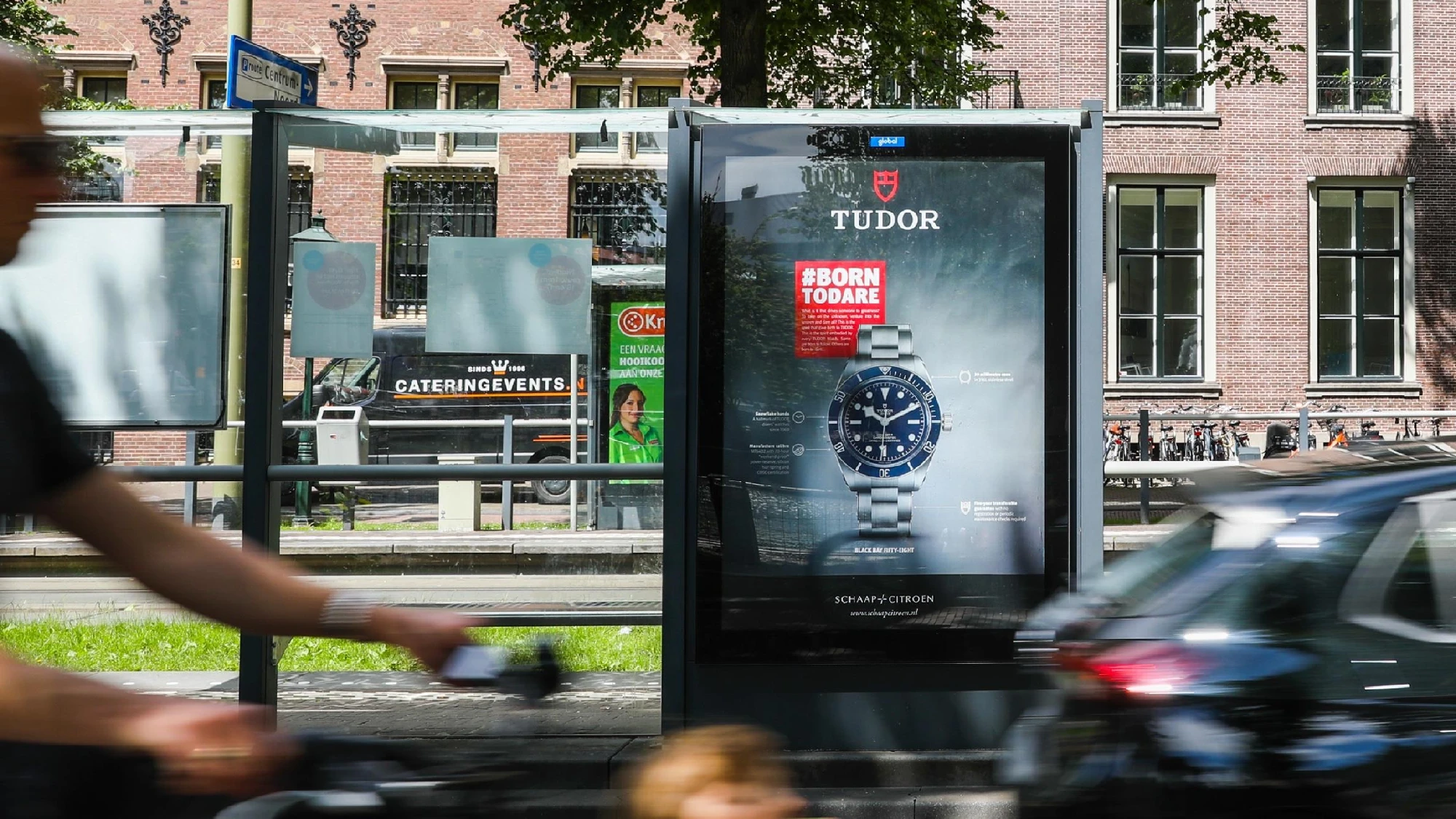 Street furniture advertising in the Netherlands: a bus shelter screen shows a Tudor watch with the line Born to Dare.