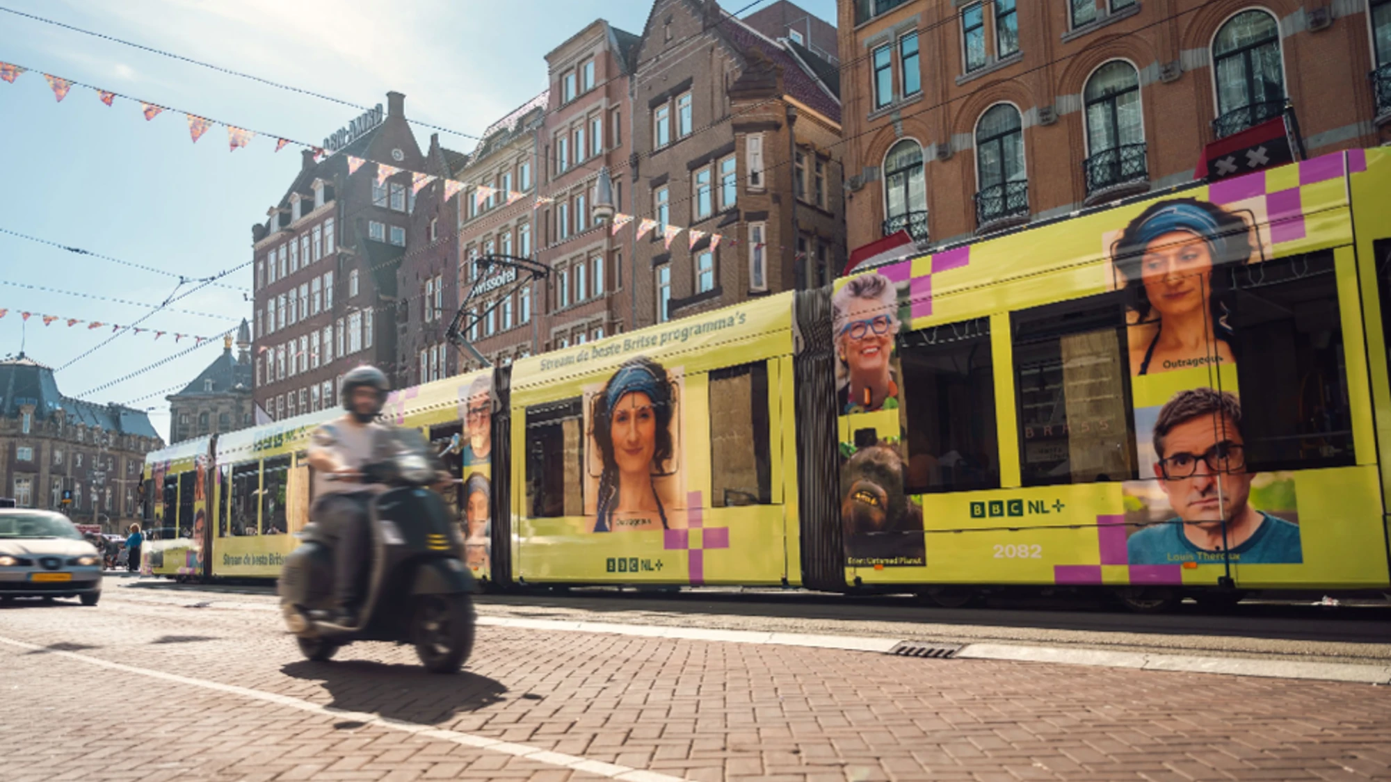 Tram advertising in the Netherlands: a yellow tram wrapped with BBC NL+ portraits passes brick canal houses.