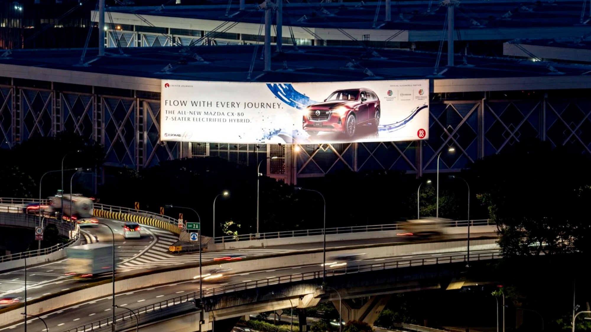 Billboard advertising in Singapore: a gantry board over a highway at night advertises the all-new Mazda CX-80, reading Flow with every journey.