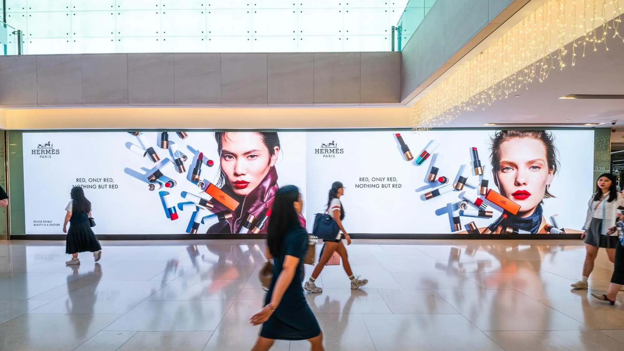 Large format advertising in a Singapore mall: a wide Hermès lightbox reads Red, only red, nothing but red, with lipstick stills and two models.