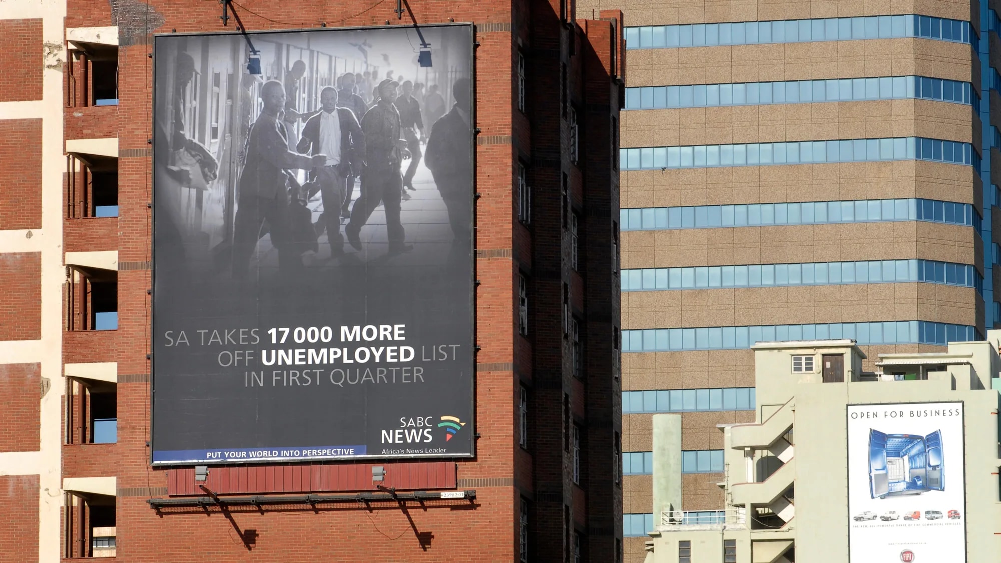 Building banner advertising in Durban, South Africa: a banner on a brick building carries an SABC News line, SA takes 17,000 more off the unemployed list.