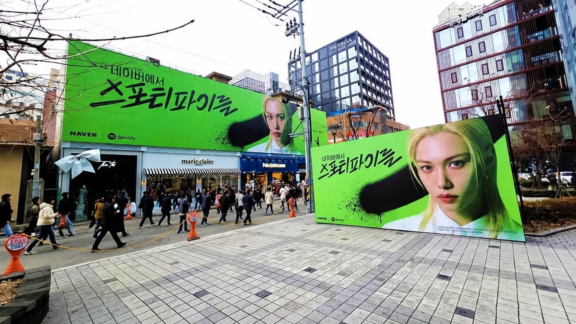 Billboard advertising in South Korea: green Naver and Spotify boards show a blonde artist on a busy shopping street.