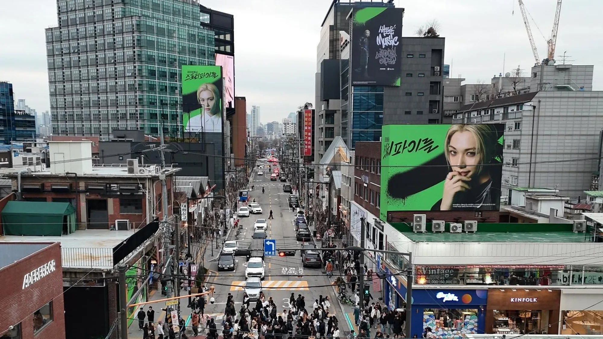 Digital out-of-home advertising in South Korea: screens above a shopping street include a green Spotify portrait of a blonde artist.
