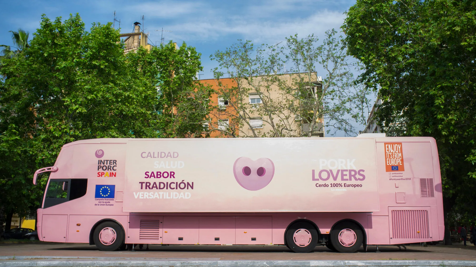Bus advertising in Spain: a pink Interporc Spain bus carries a Pork Lovers campaign along a tree-lined street.