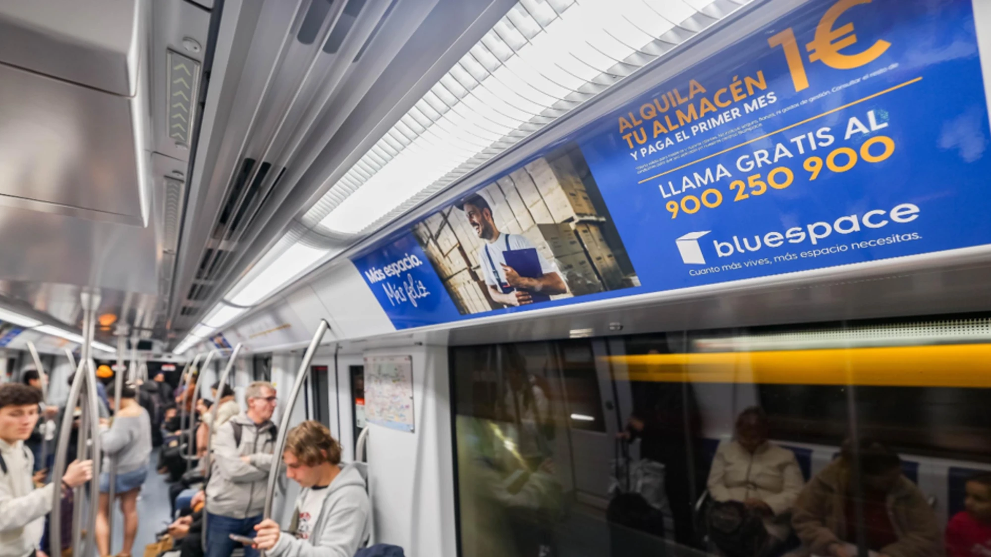 Rail advertising in Spain: a Bluespace advert for storage rental runs above the windows of a busy train carriage.