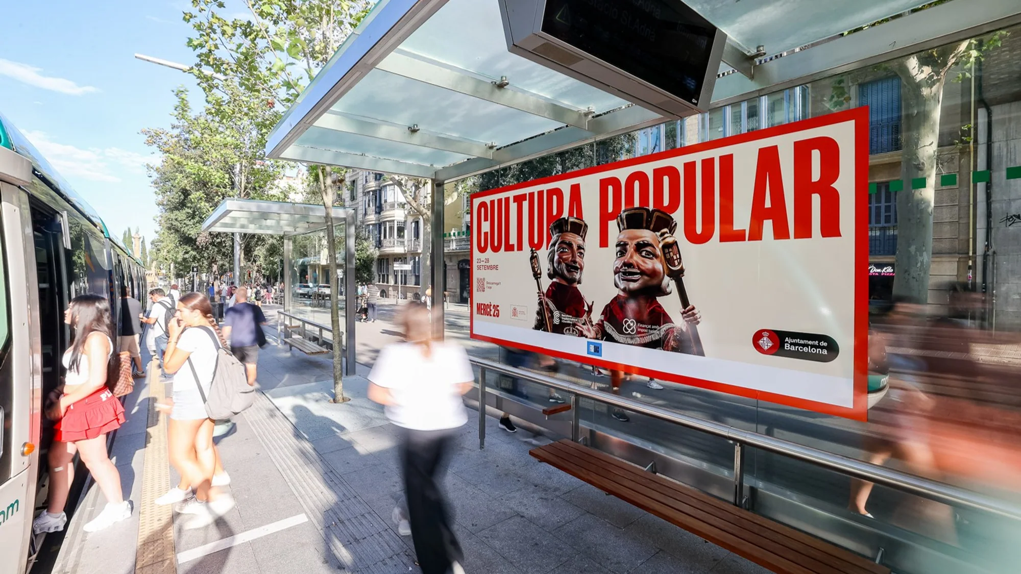 Street furniture advertising in Barcelona, Spain: a Cultura Popular poster for Mercè 25, from Ajuntament de Barcelona, is fixed to a tram stop shelter.