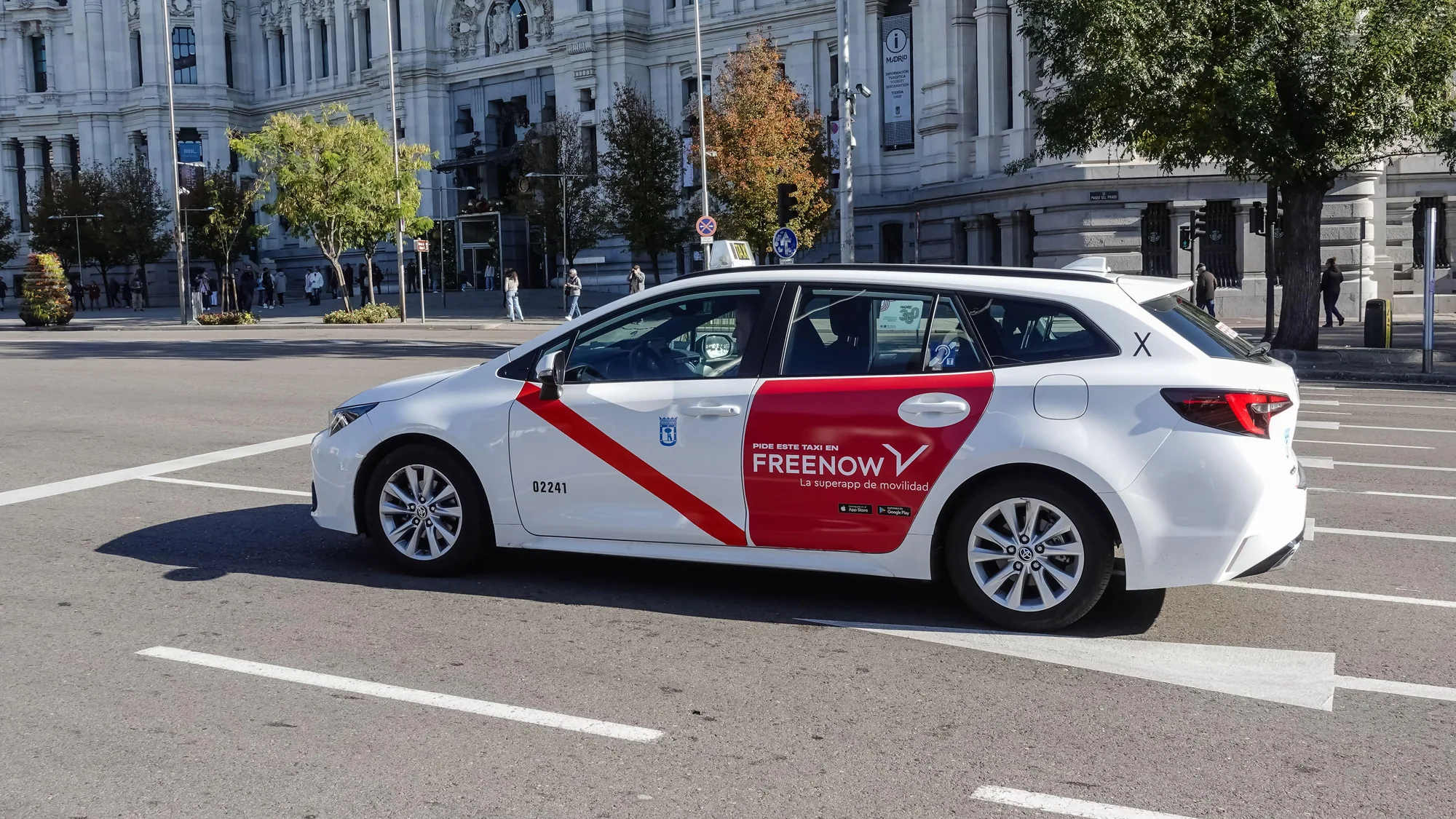 Taxi advertising in Madrid, Spain: a white and red FREENOW taxi drives past a grand stone building.