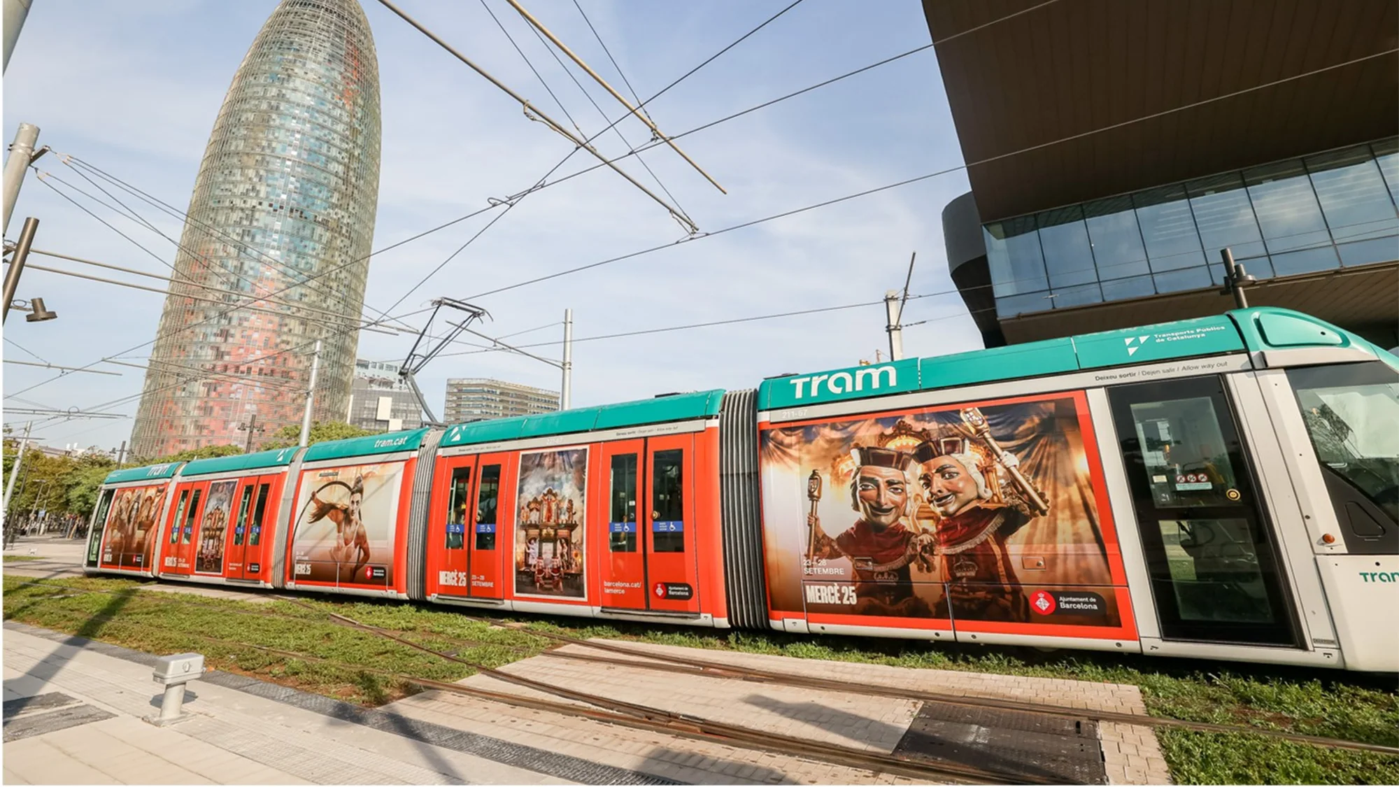 Tram advertising in Barcelona, Spain: a tram wrapped for Mercè 25 passes Torre Glòries, with Ajuntament de Barcelona on the side.
