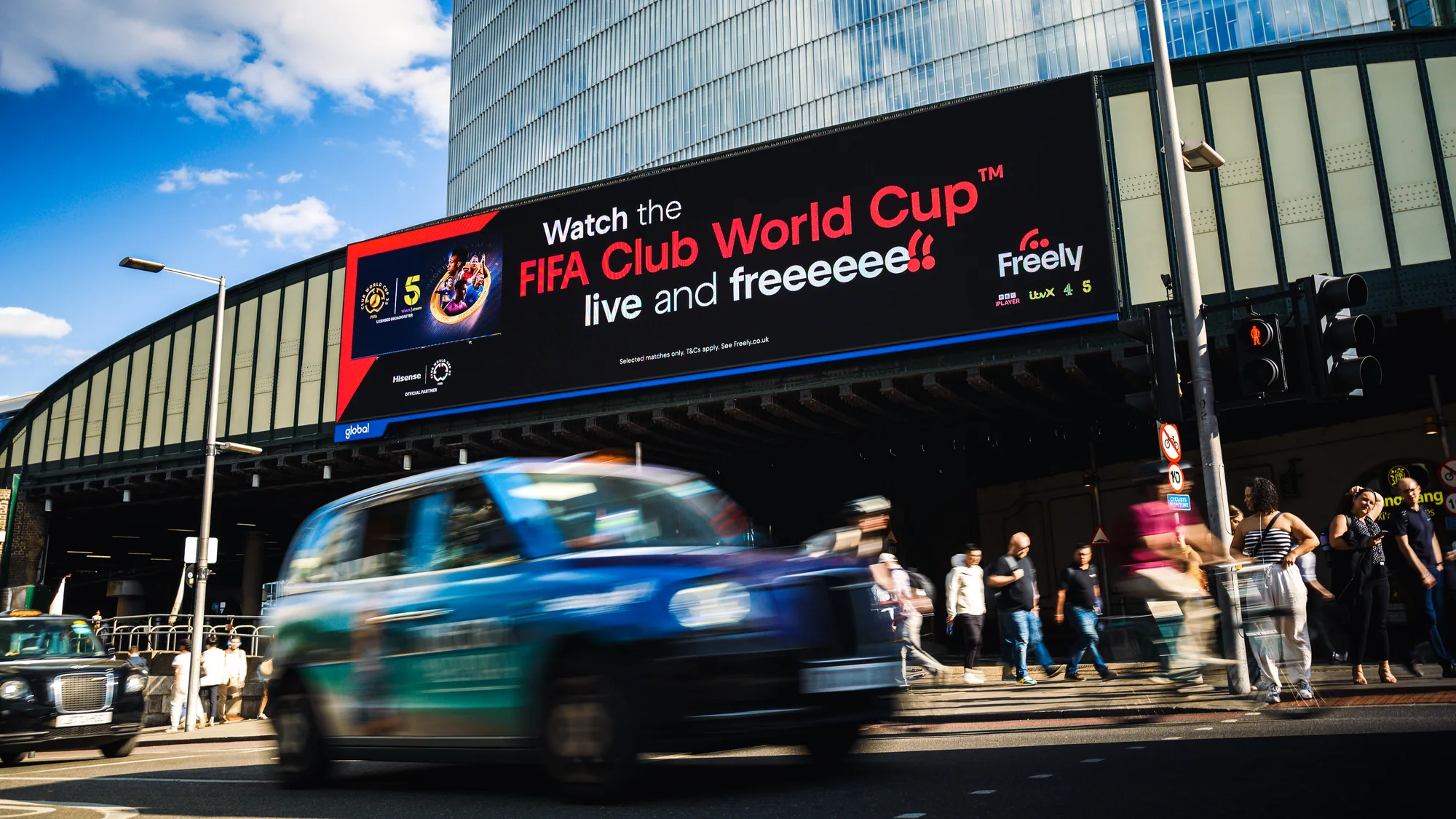 Digital out-of-home advertising in London, in the United Kingdom: a roadside screen says watch the FIFA Club World Cup live and free on Freely, above a passing taxi.