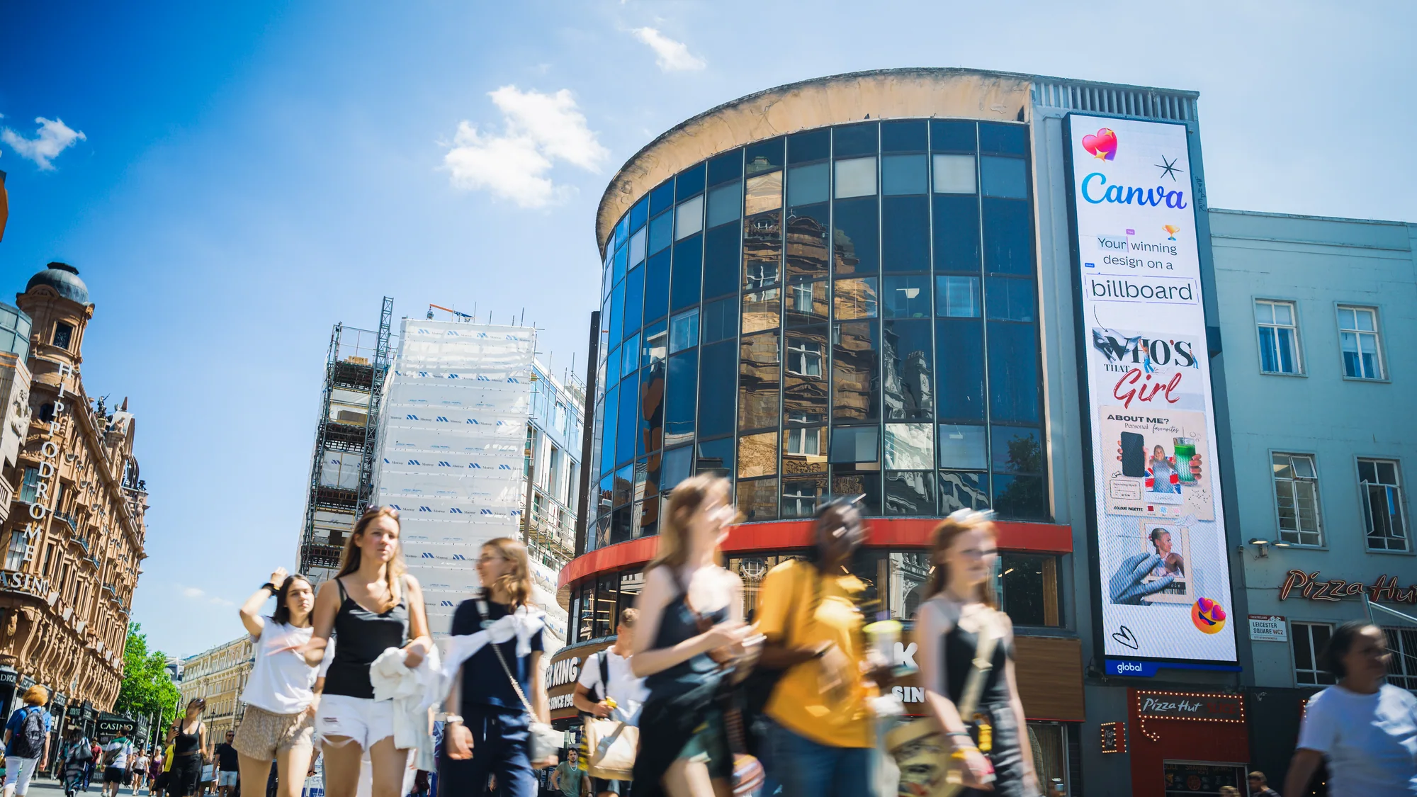 Large format billboard advertising in the United Kingdom: a tall Canva banner shows Who's That Girl and Your winning design on a corner building.