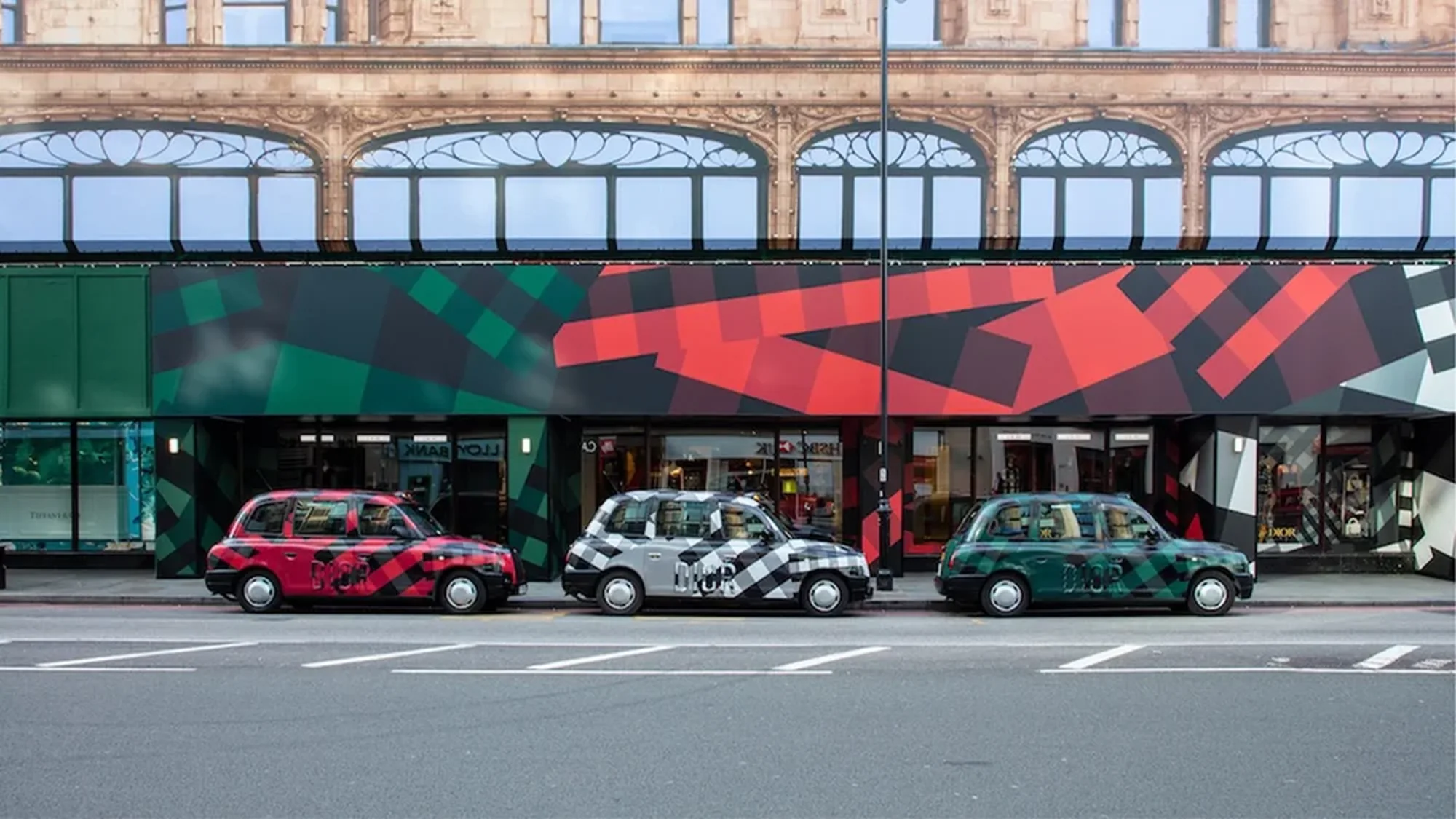 Taxi advertising in London, in the United Kingdom: three black cabs in red, silver and green geometric wraps are parked outside a matching shopfront.
