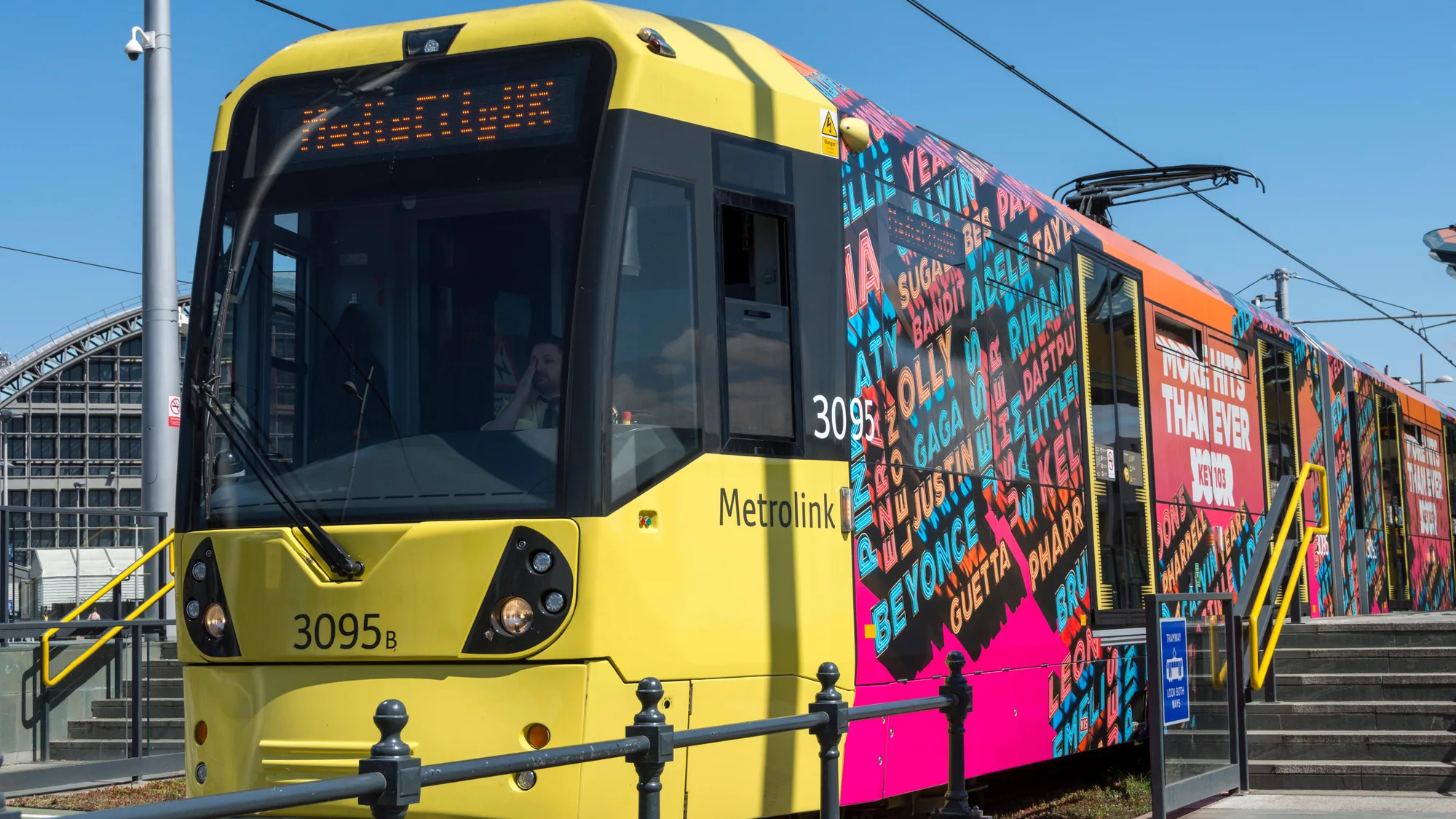 Tram advertising at Deansgate-Castlefield in Manchester, in the United Kingdom: a yellow Metrolink tram wrapped for Key 103 reads More hits than ever.