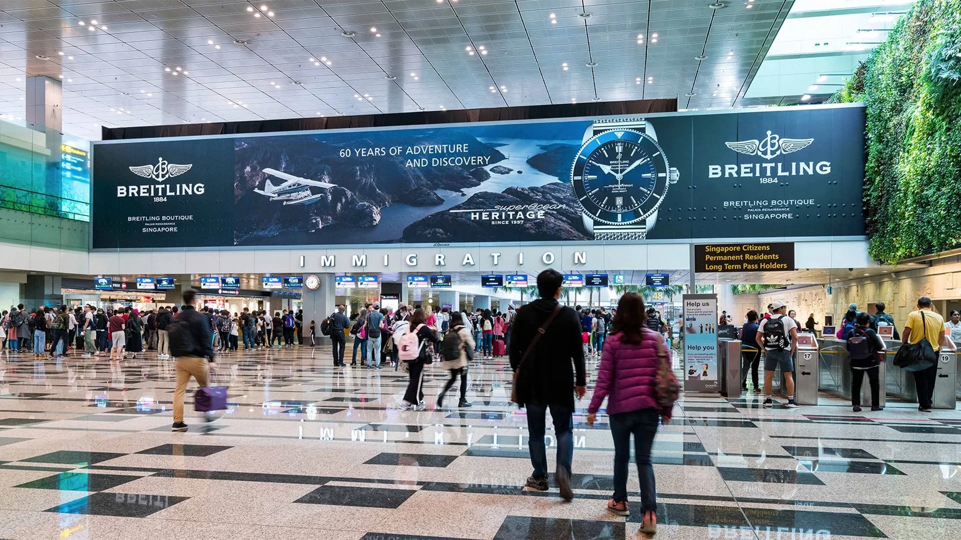 Airport advertising at Singapore Changi Airport: travellers walk towards immigration beneath a Breitling banner.