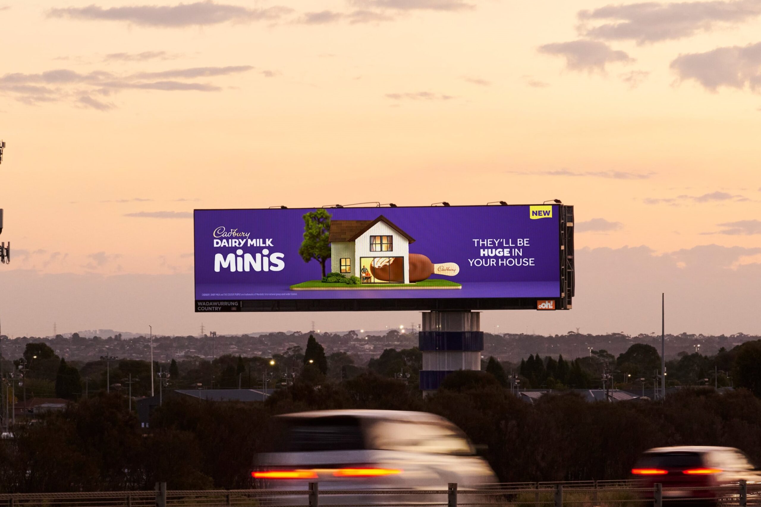 Roadside billboard advertising: a Cadbury Dairy Milk Minis board stands above a highway at sunset.