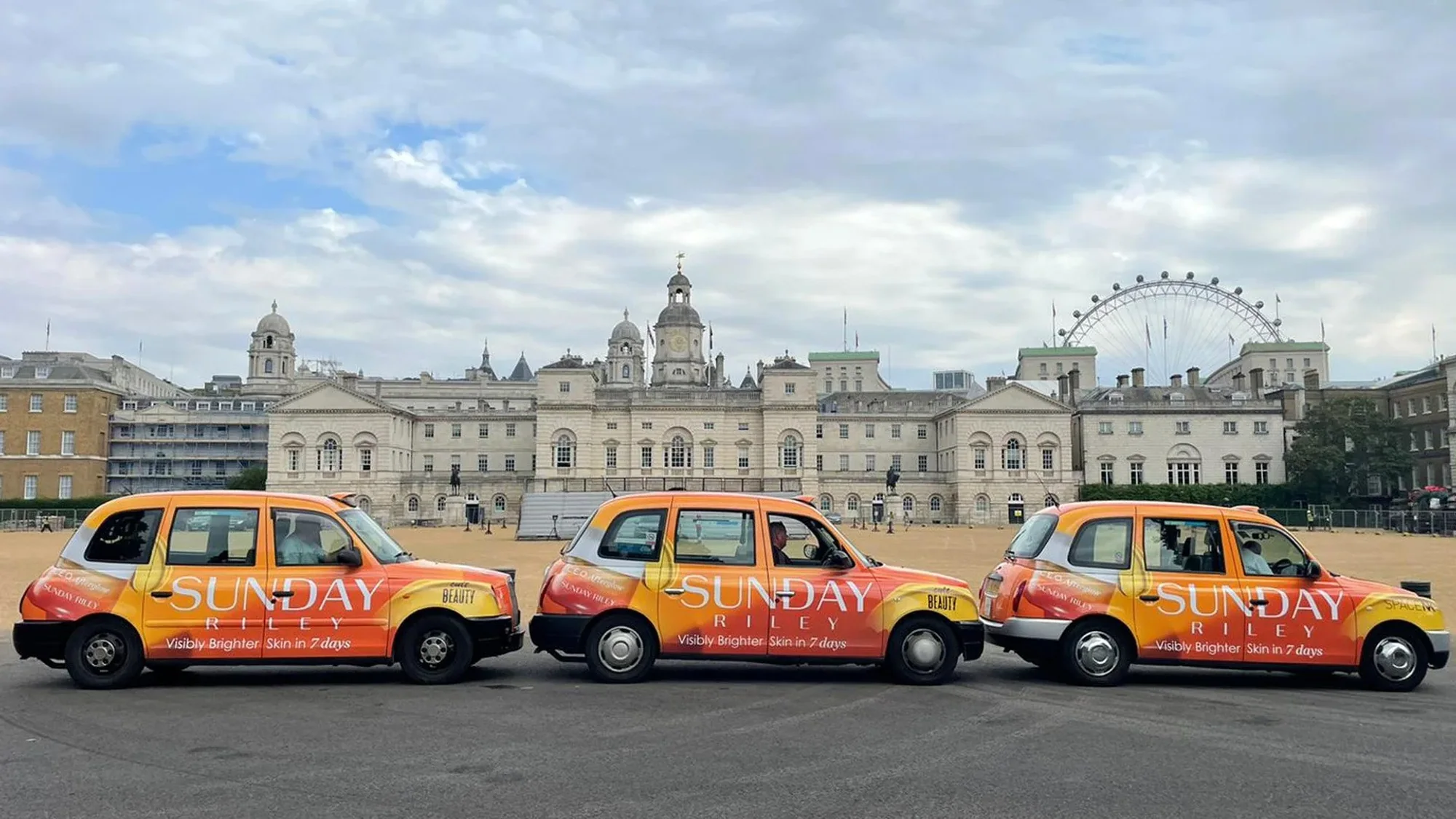 Taxi advertising in London, in the United Kingdom: three Sunday Riley taxis stand before a white building and the London Eye.