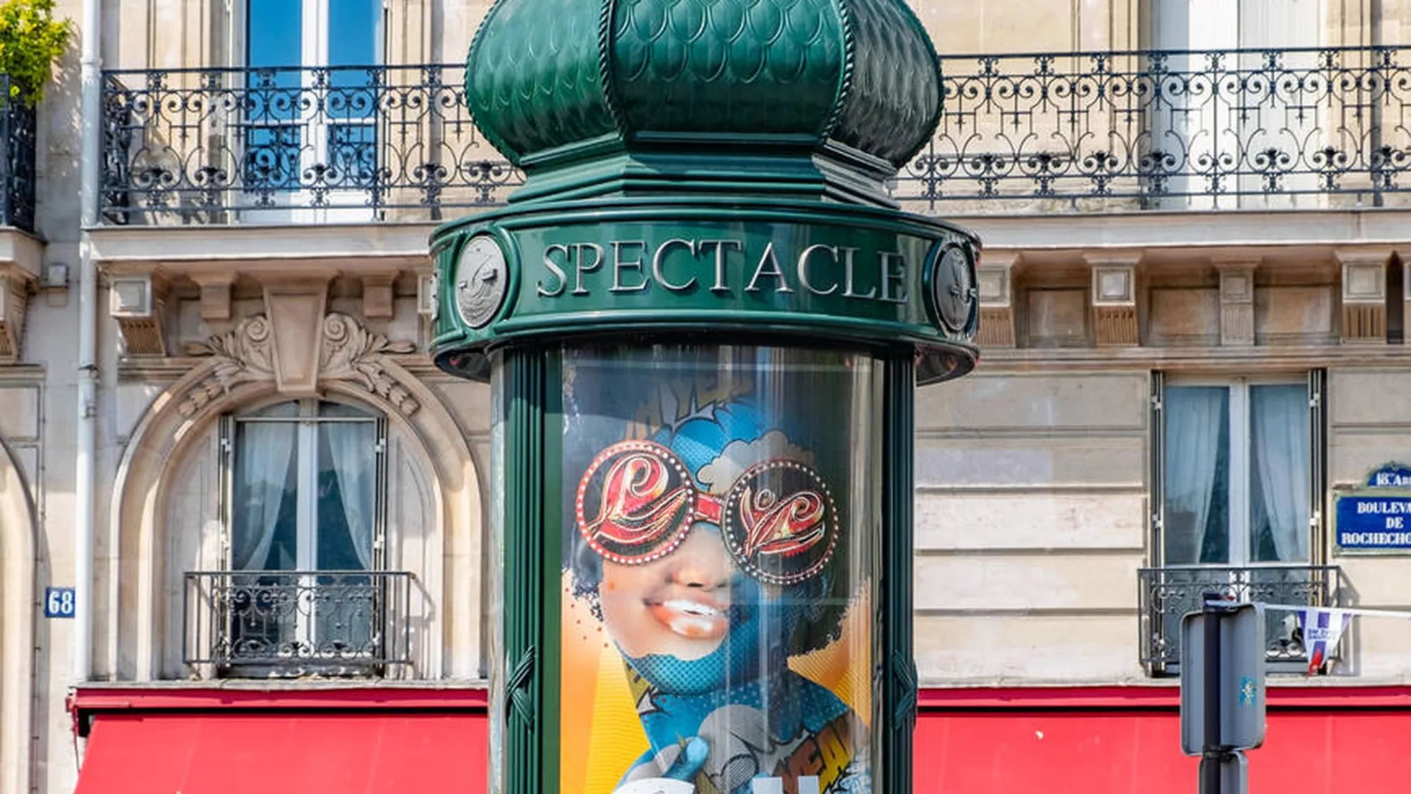 Street furniture advertising in Paris, France: a green spectacle column on Boulevard de Rochechouart displays a poster of a woman wearing Love sunglasses.
