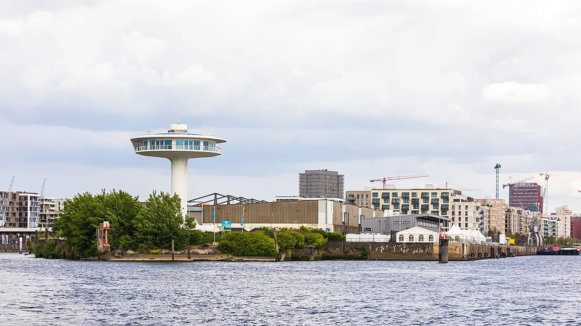 The Lighthouse Zero tower in Hamburg, Germany: a white disc-topped tower stands on a harbour peninsula, with cranes and new apartment blocks behind it.
