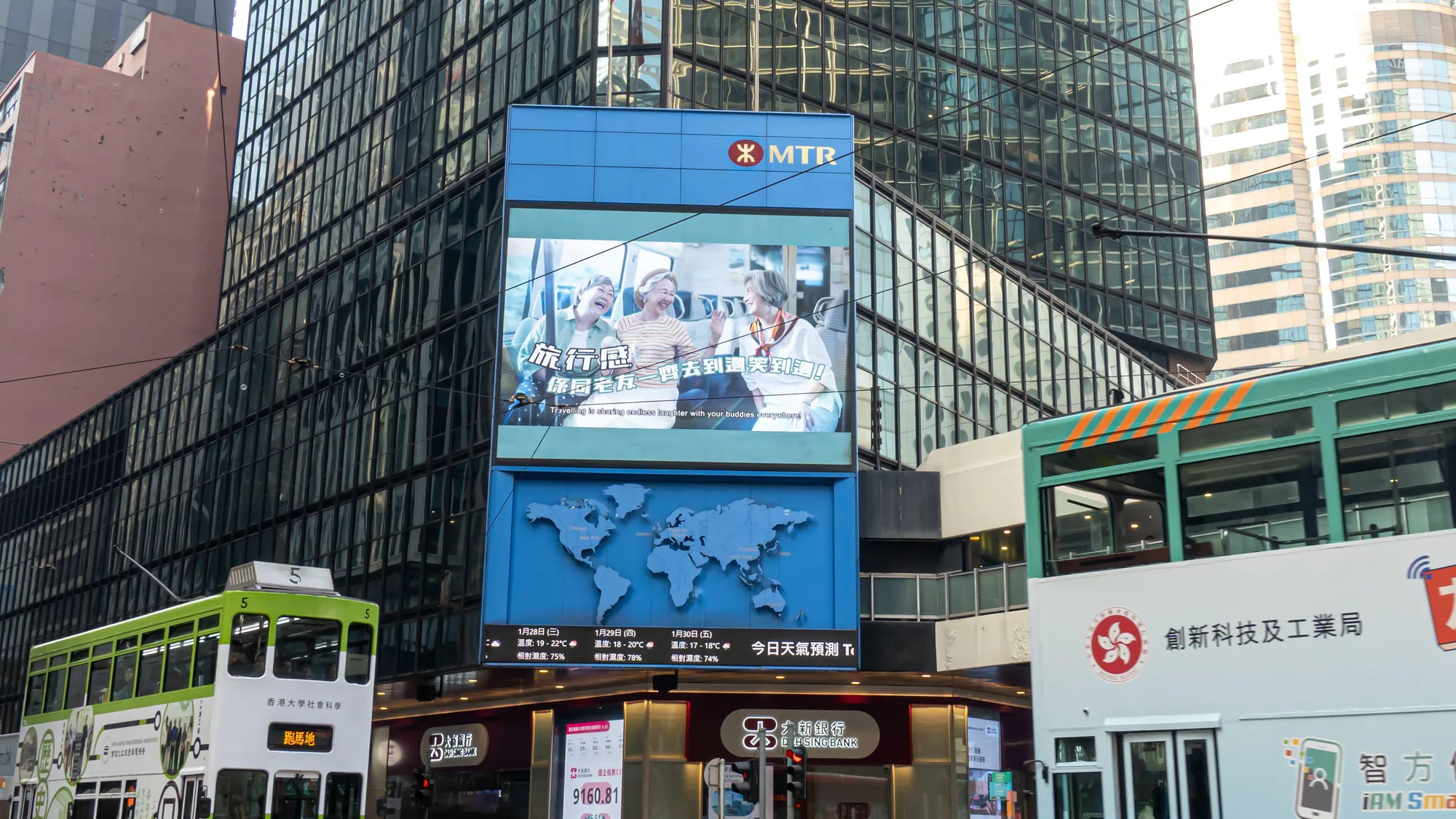 Digital billboard advertising in Central, Hong Kong: pedestrians cross a junction under a curved screen and a Blue Coast board, beside the Airport Express sign.