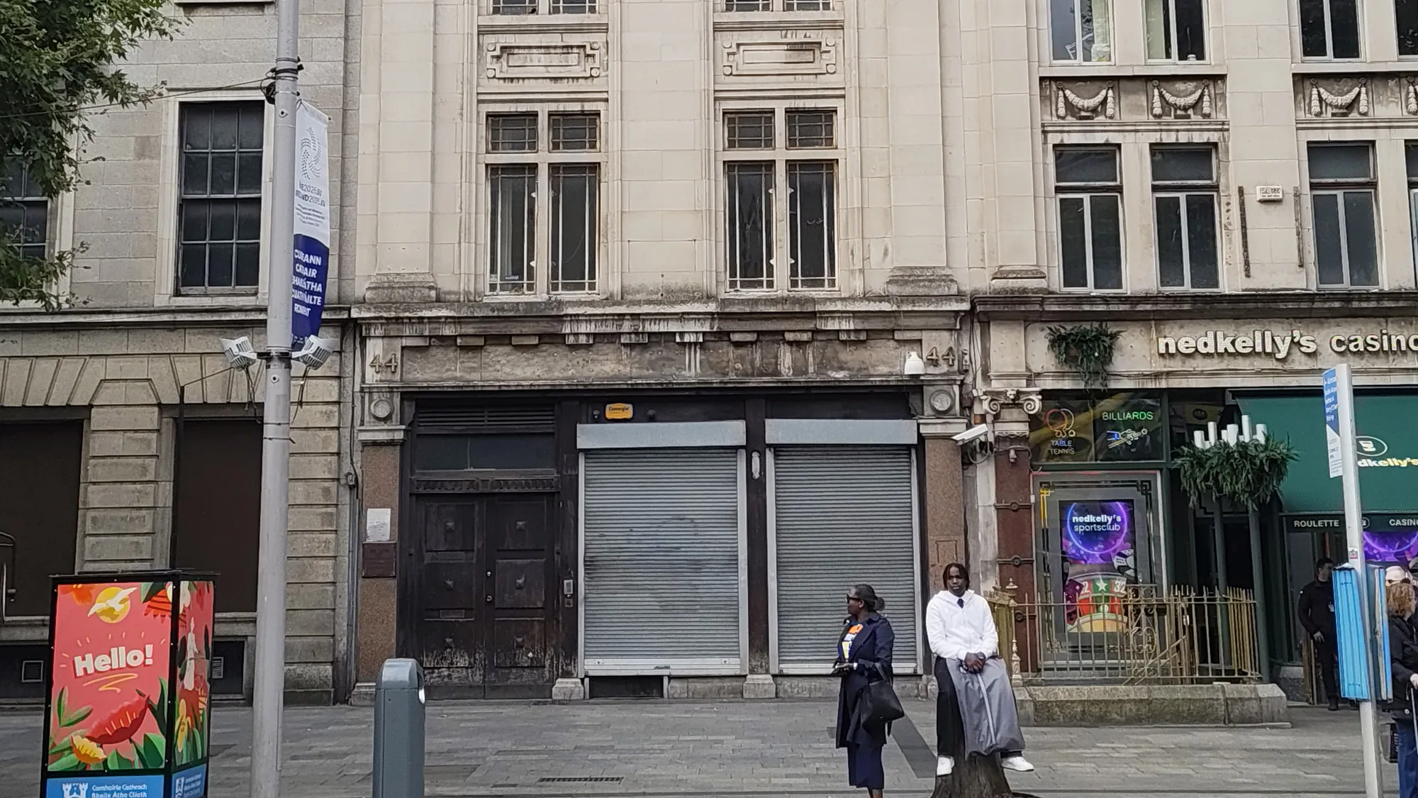 A small poster reading Hello stands on a Dublin pavement, outside shuttered shopfronts and a Ned Kelly's casino.