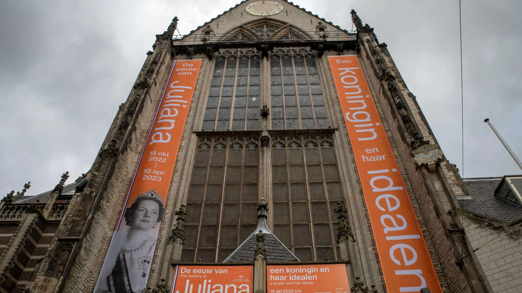 Building banner advertising at the Nieuwe Kerk in Amsterdam, the Netherlands: orange banners for the exhibition De eeuw van Juliana hang on the stained-glass facade.